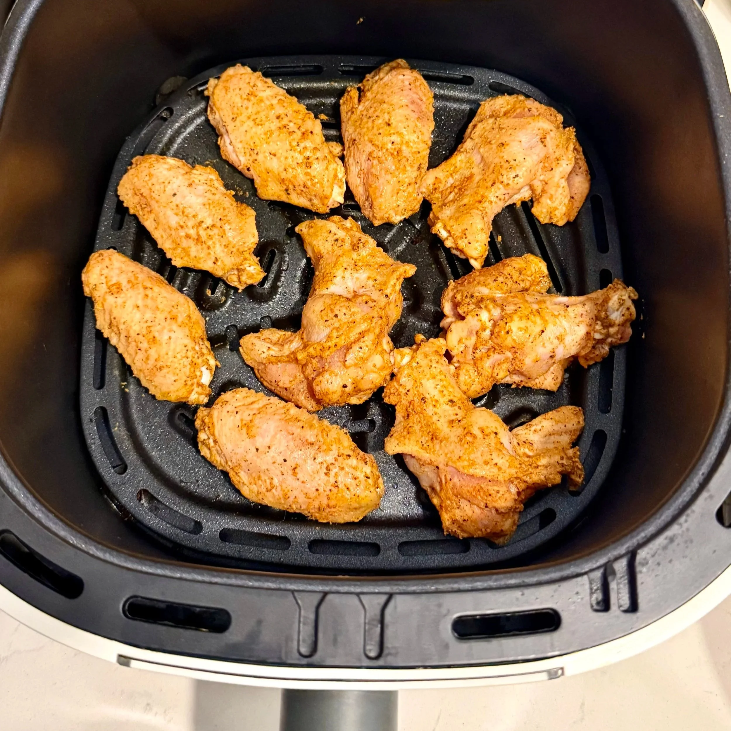 Seasoned chicken wings arranged in an air fryer basket ready to cook