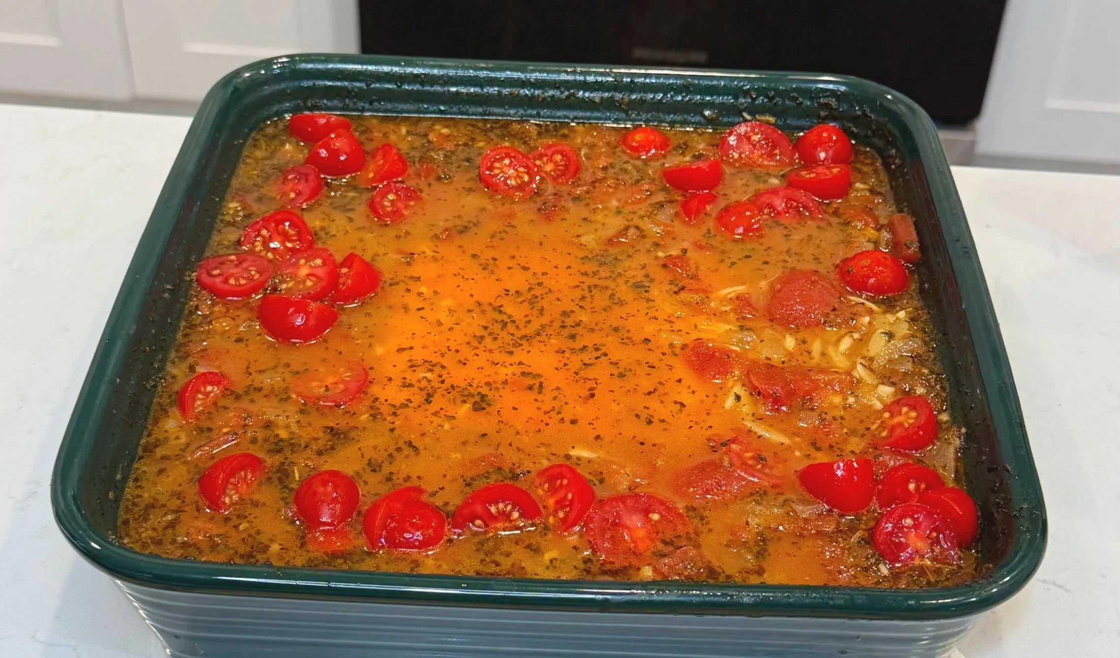 Uncooked orzo pasta stirred into tomato sauce in a baking dish