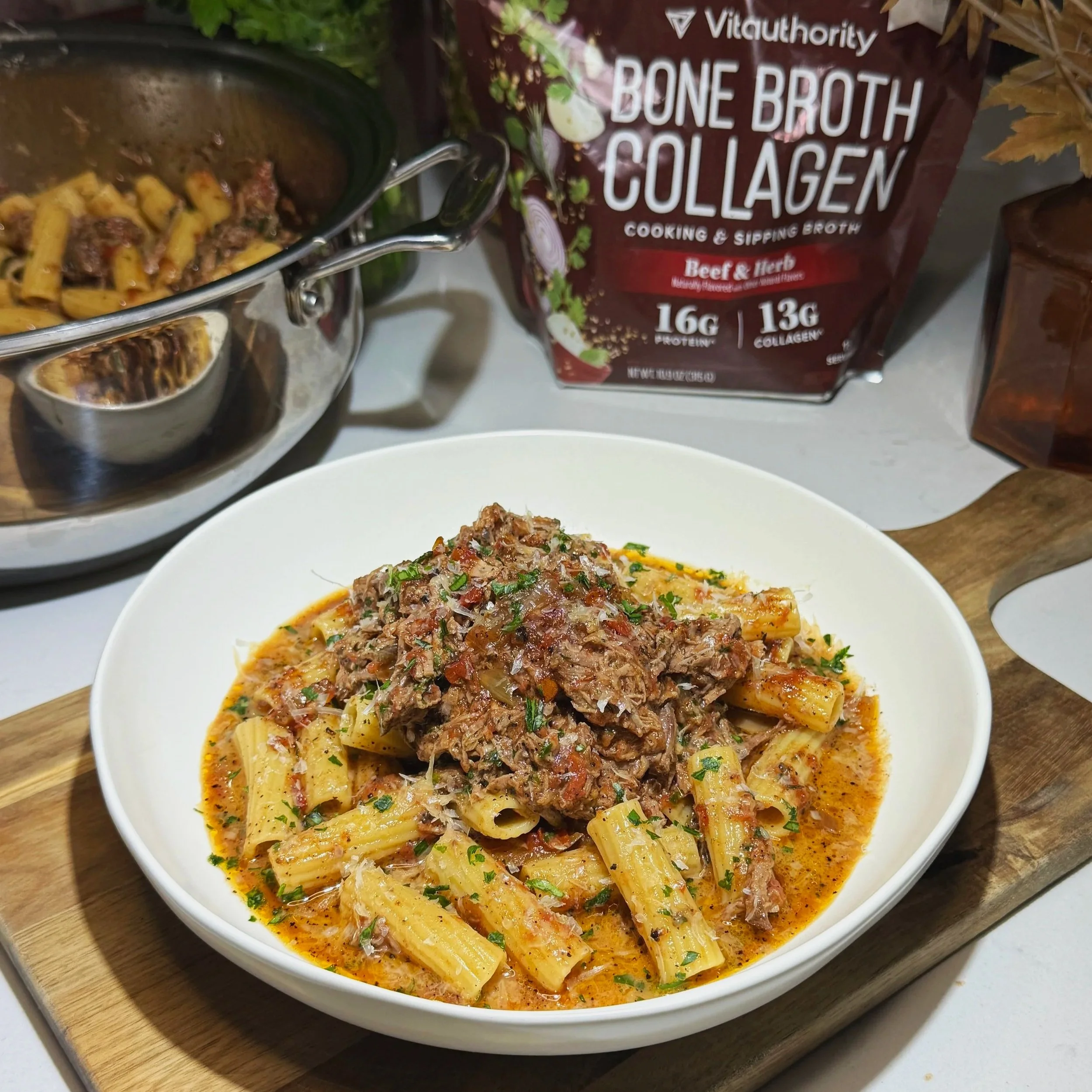 Close‑up of plated slow cooker beef brisket pasta with rigatoni, shredded beef, and parsley garnish on a wooden board