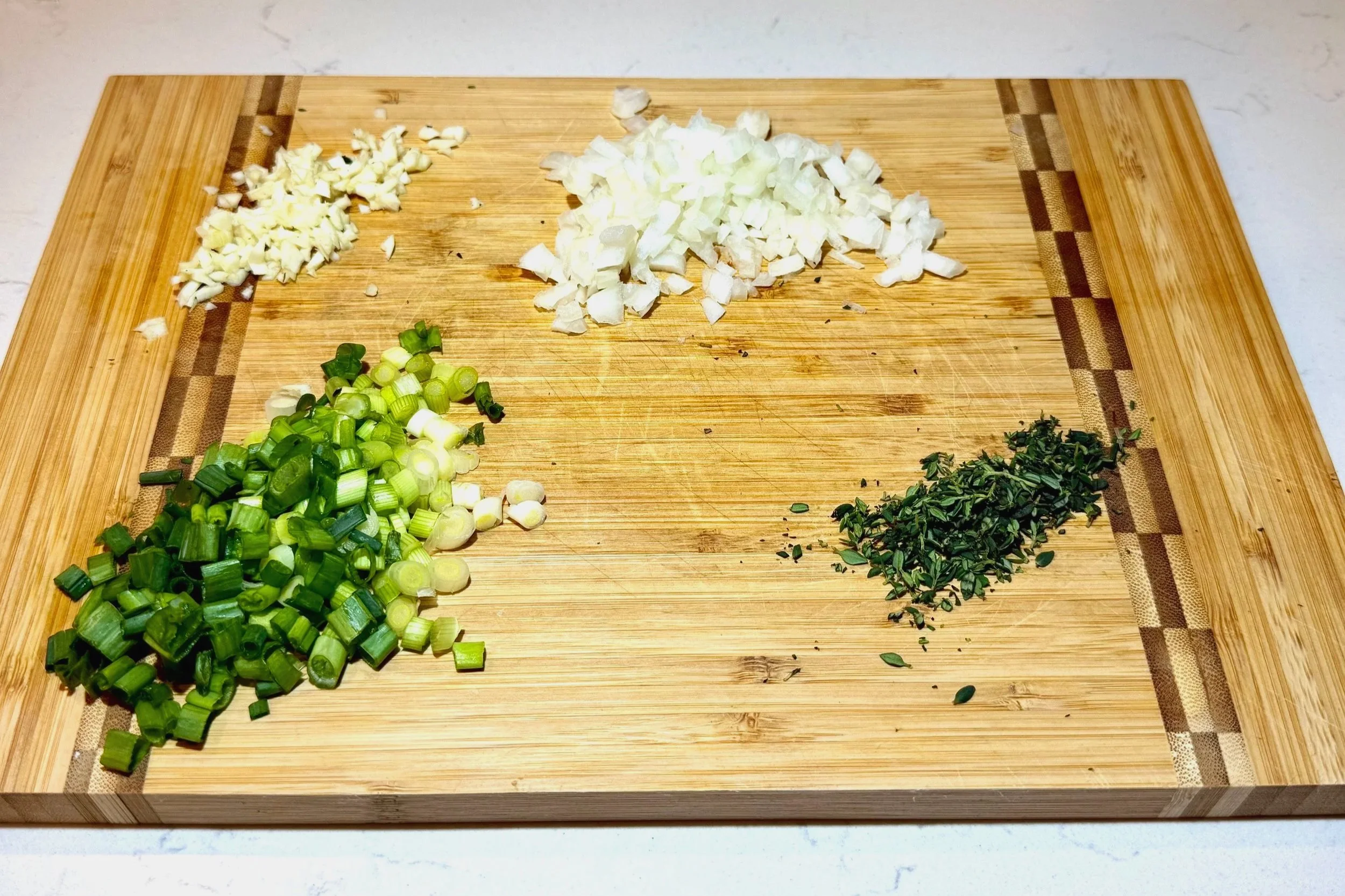 Ingredients for Jamaican saltfish fritters laid out on a cutting board including scallions, onion, garlic, Scotch bonnet, and saltfish.