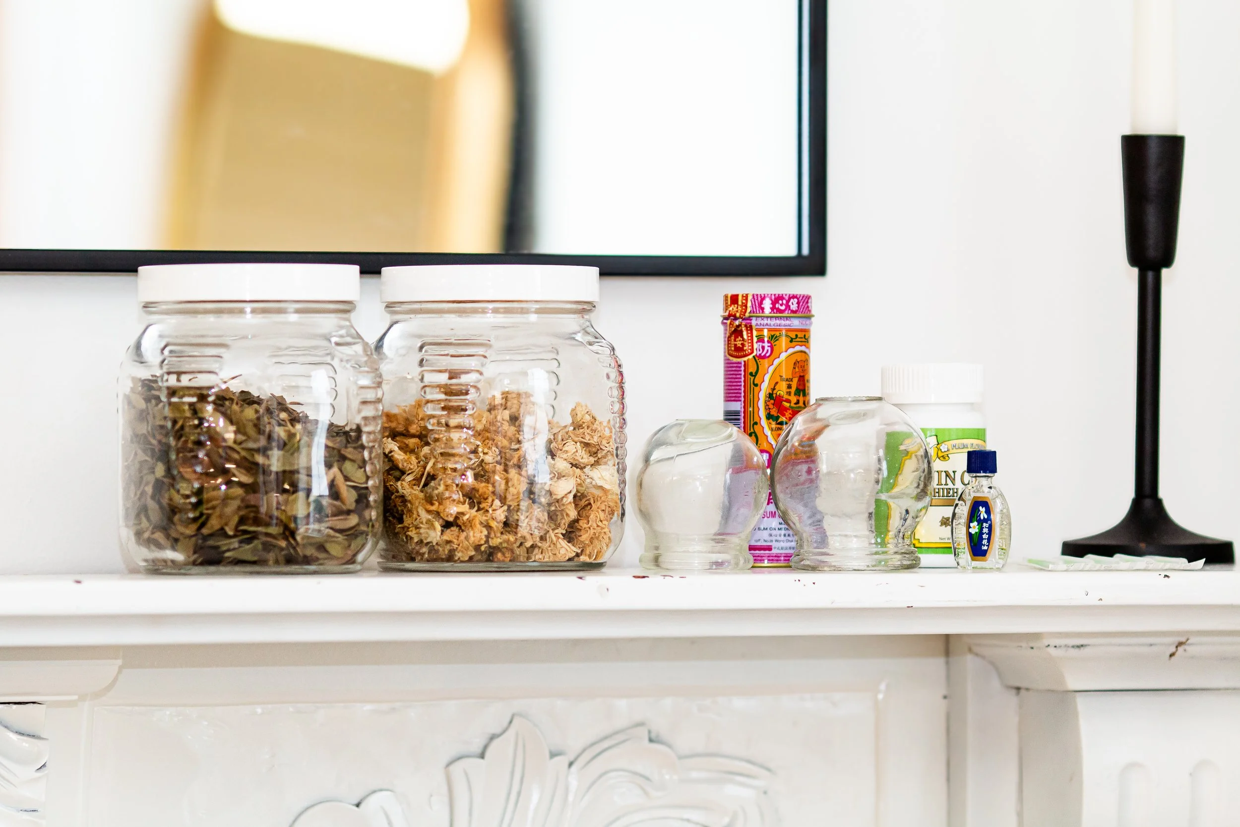 Glass jars filled with dried herbs and wellness supplies displayed on a white shelf.