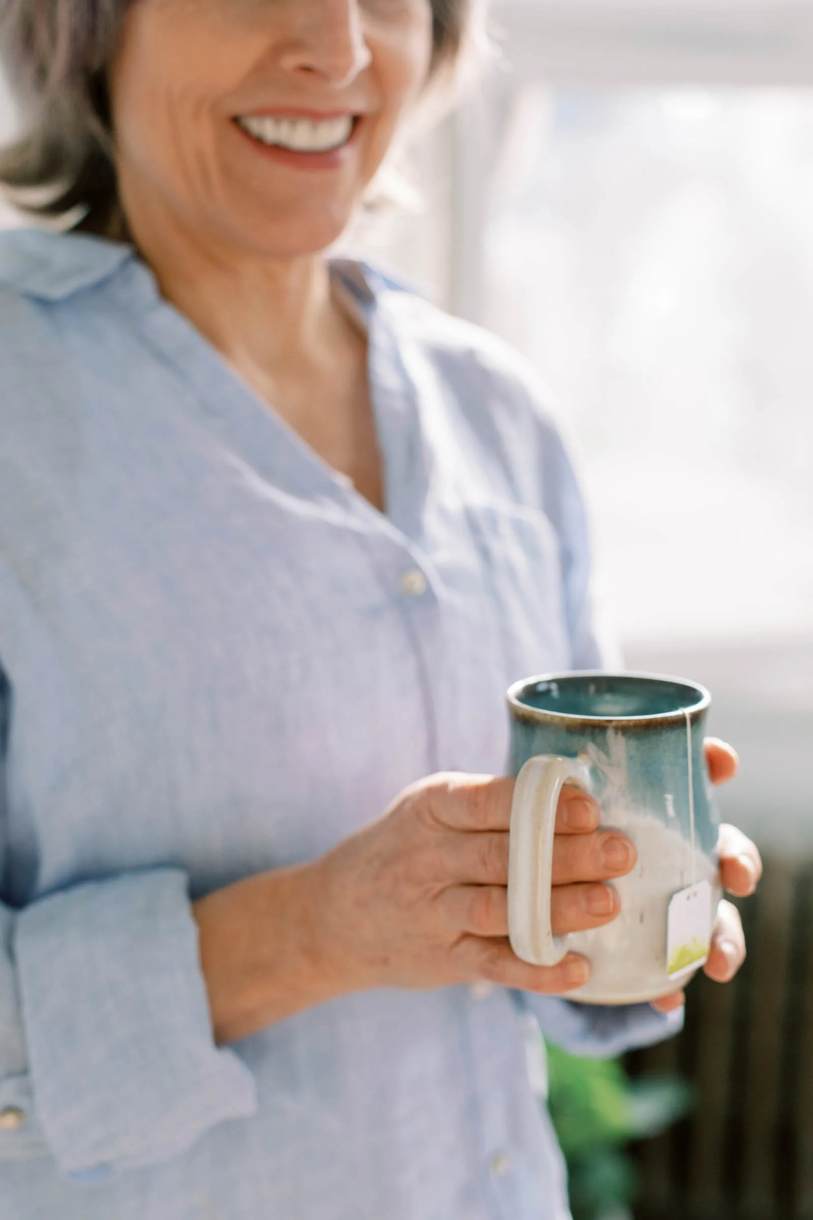 Woman holding a ceramic mug in soft natural light while wearing a light blue shirt.