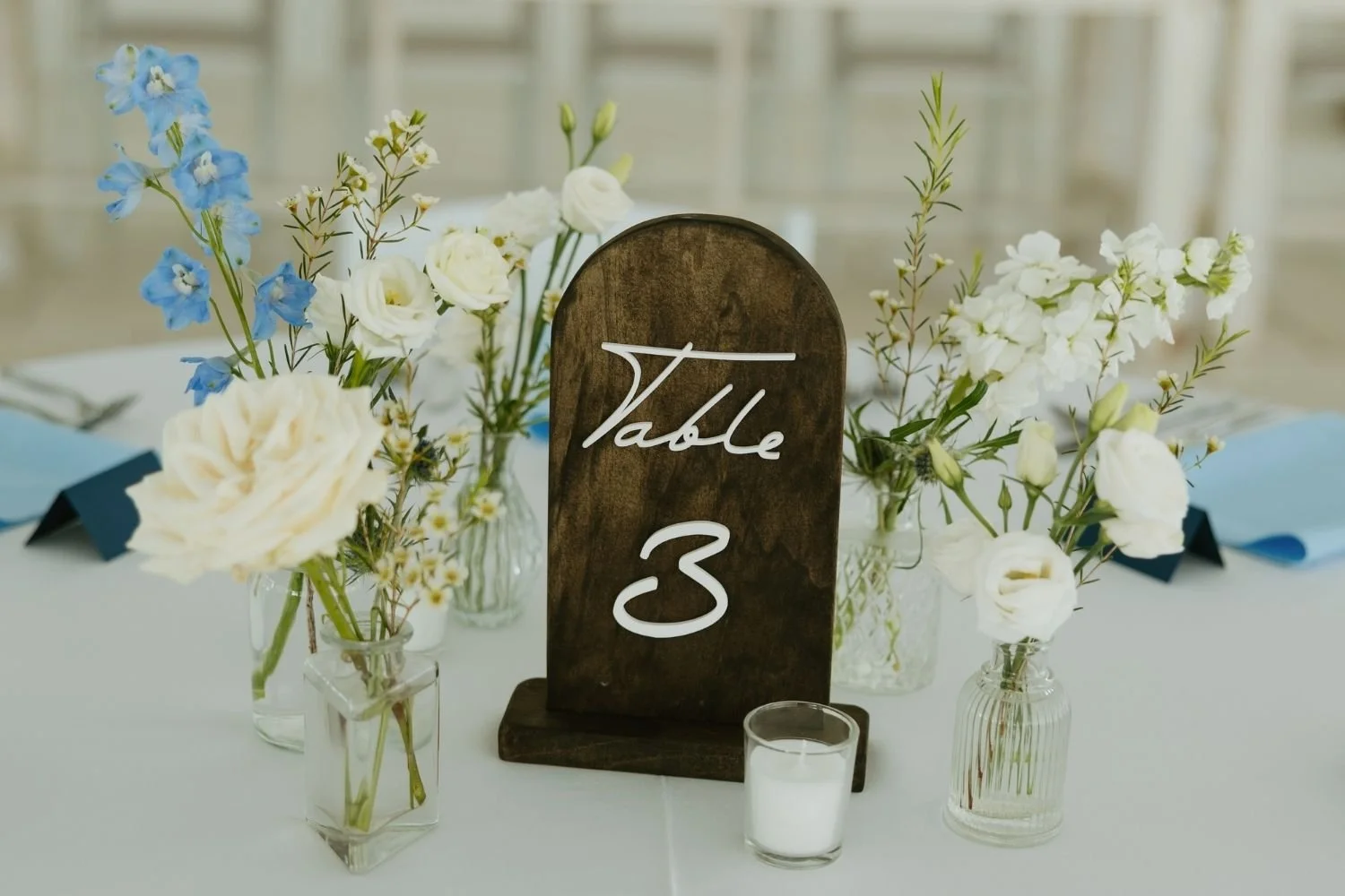 Centerpiece design on table with bud vases of white and blue flowers and a table number