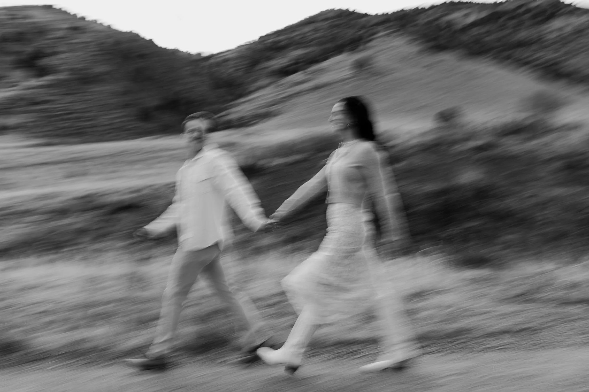A blurry black and white photo of a man and woman walking hand-in-hand outdoors.