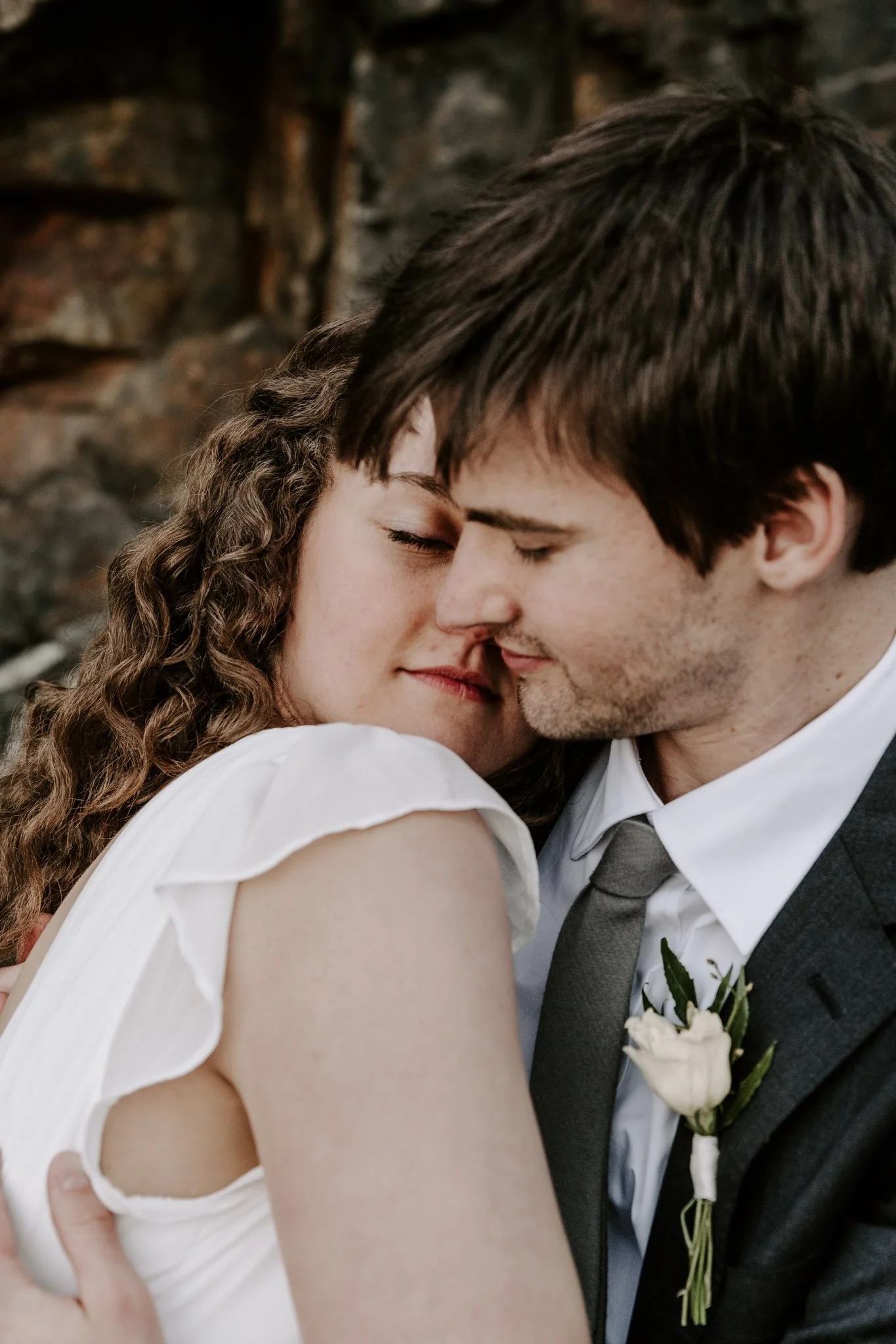 A couple with closed eyes, embracing and leaning their foreheads together, during a wedding or romantic moment outdoors.