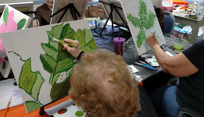 Older adults painting leaf studies during a hands-on art session in senior living.