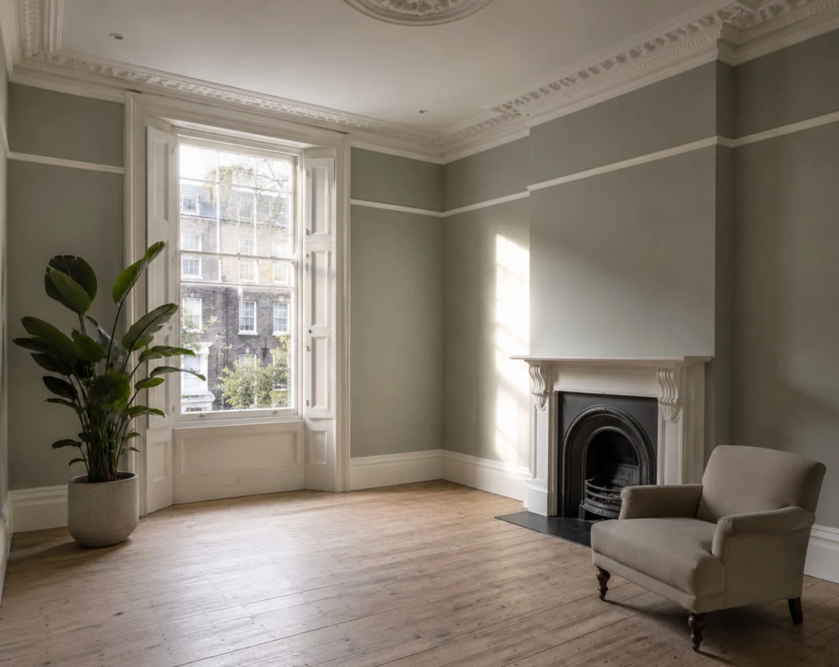 Empty room with large window, green walls, wooden floor, a fireplace, a beige armchair, and a potted plant.
