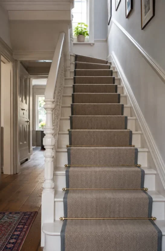 Staircase with beige carpet runner, white walls, framed pictures, and a window with a potted plant on the sill.