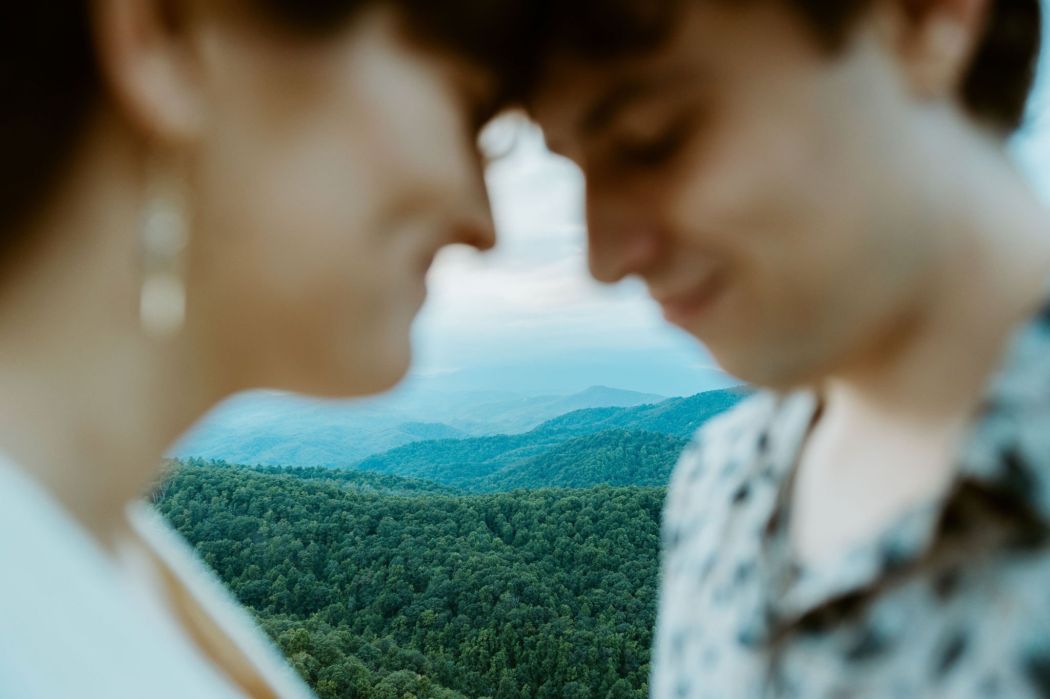 The blue ridge parkway is in focus in the distance while couple places their foreheads together after they elope in North Carolina.