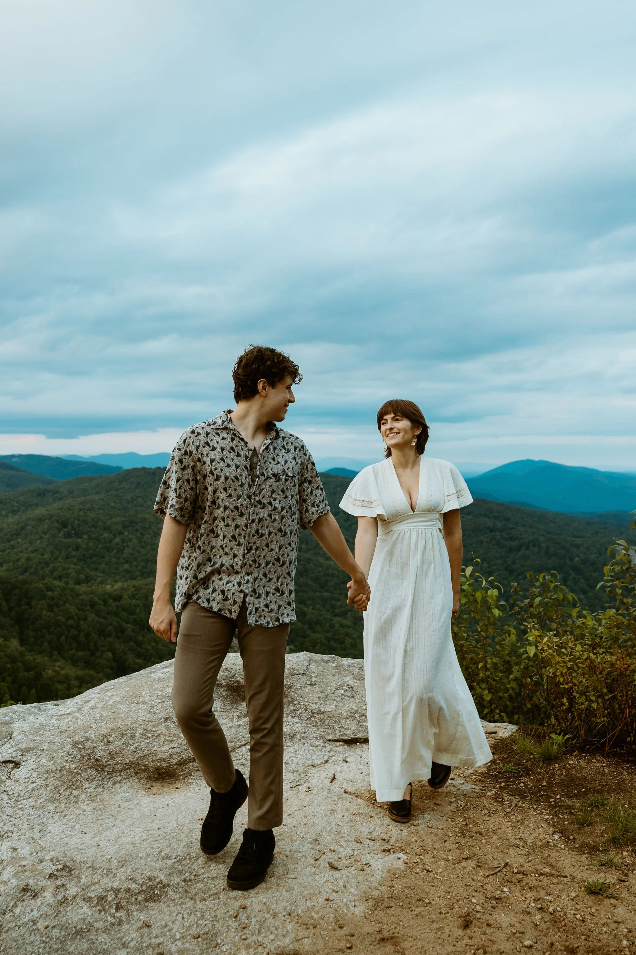 Couple walks along a boulder overlooking the blue ridge parkway.