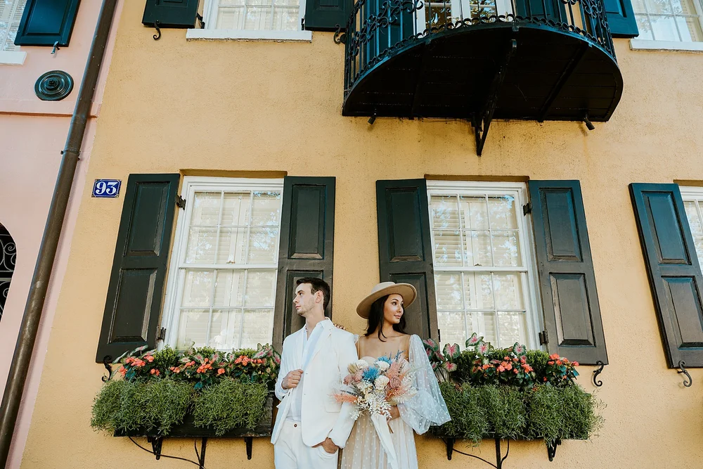 Couple poses in front of a yellow Rainbow Row house before they head to Folly Beach for their elopement