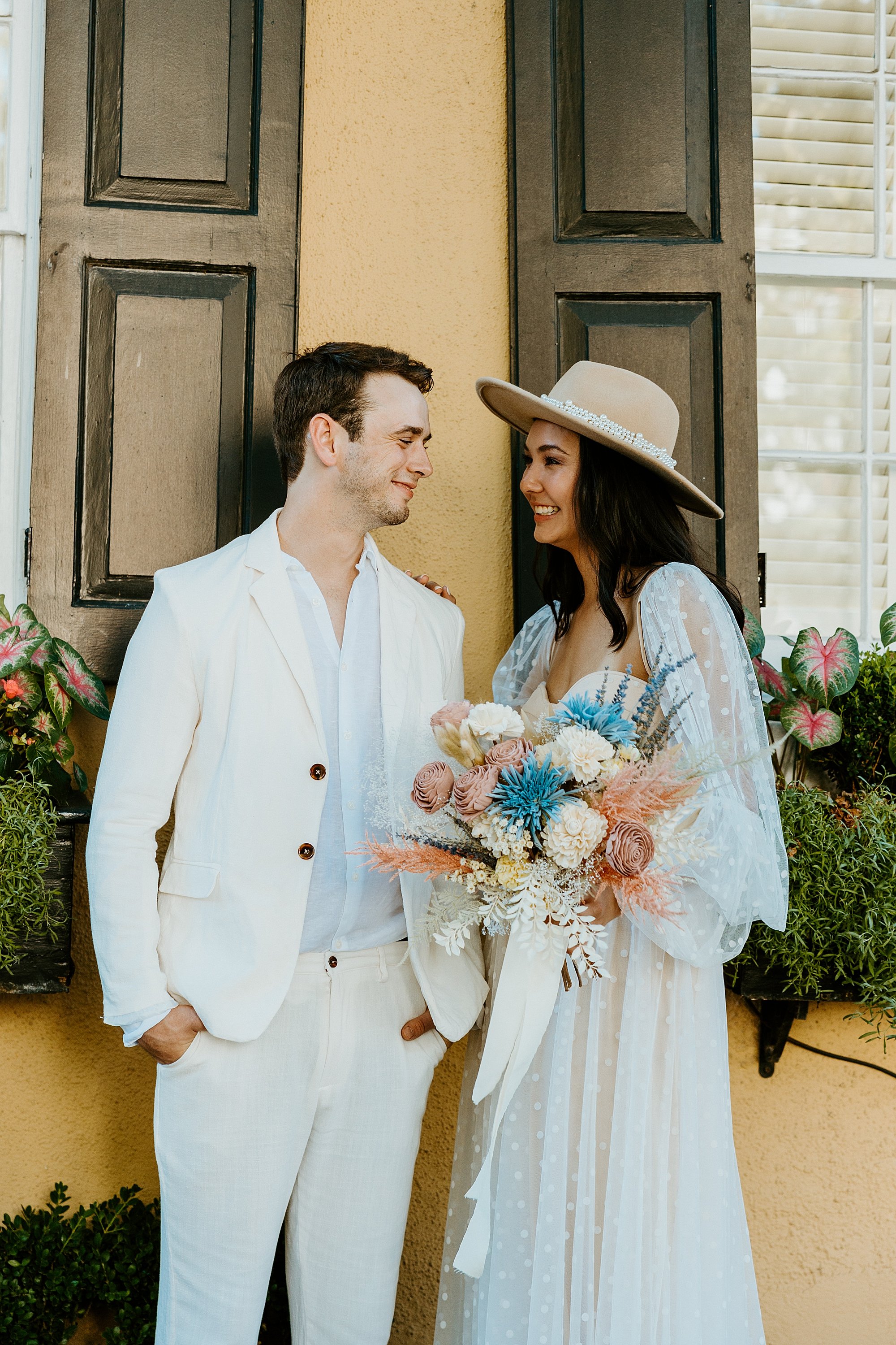 Couple stands together in front of a historic yellow house on Rainbow Row. How to elope in Charleston SC