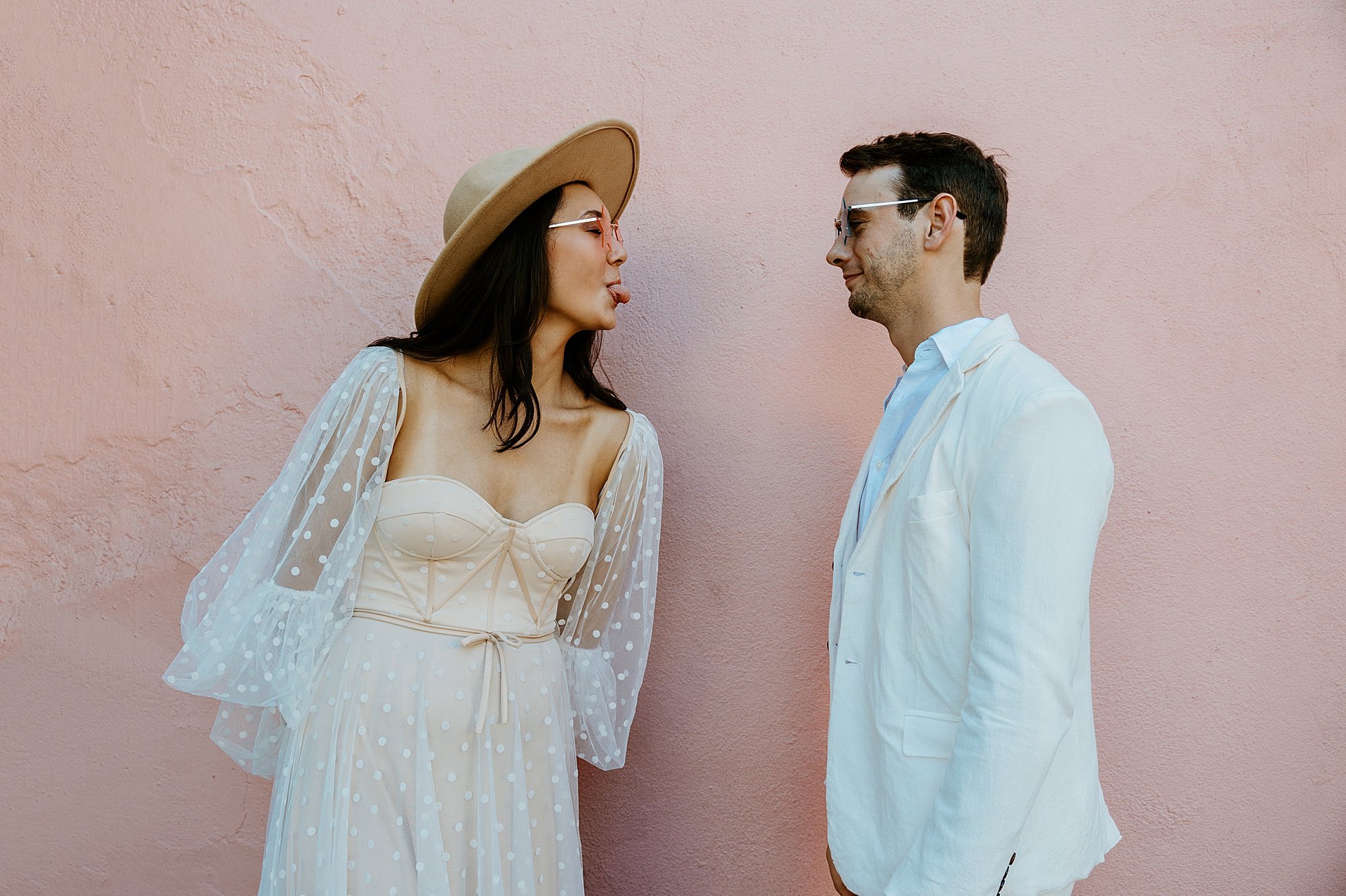 Couple makes silly faces at each other in front of a pink house on Rainbow Row