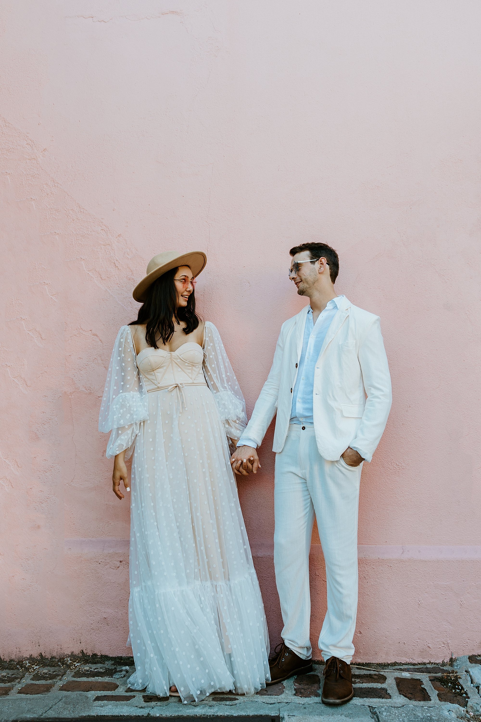 Couple stands together making faces at each other in front of a pink house on Rainbow Row