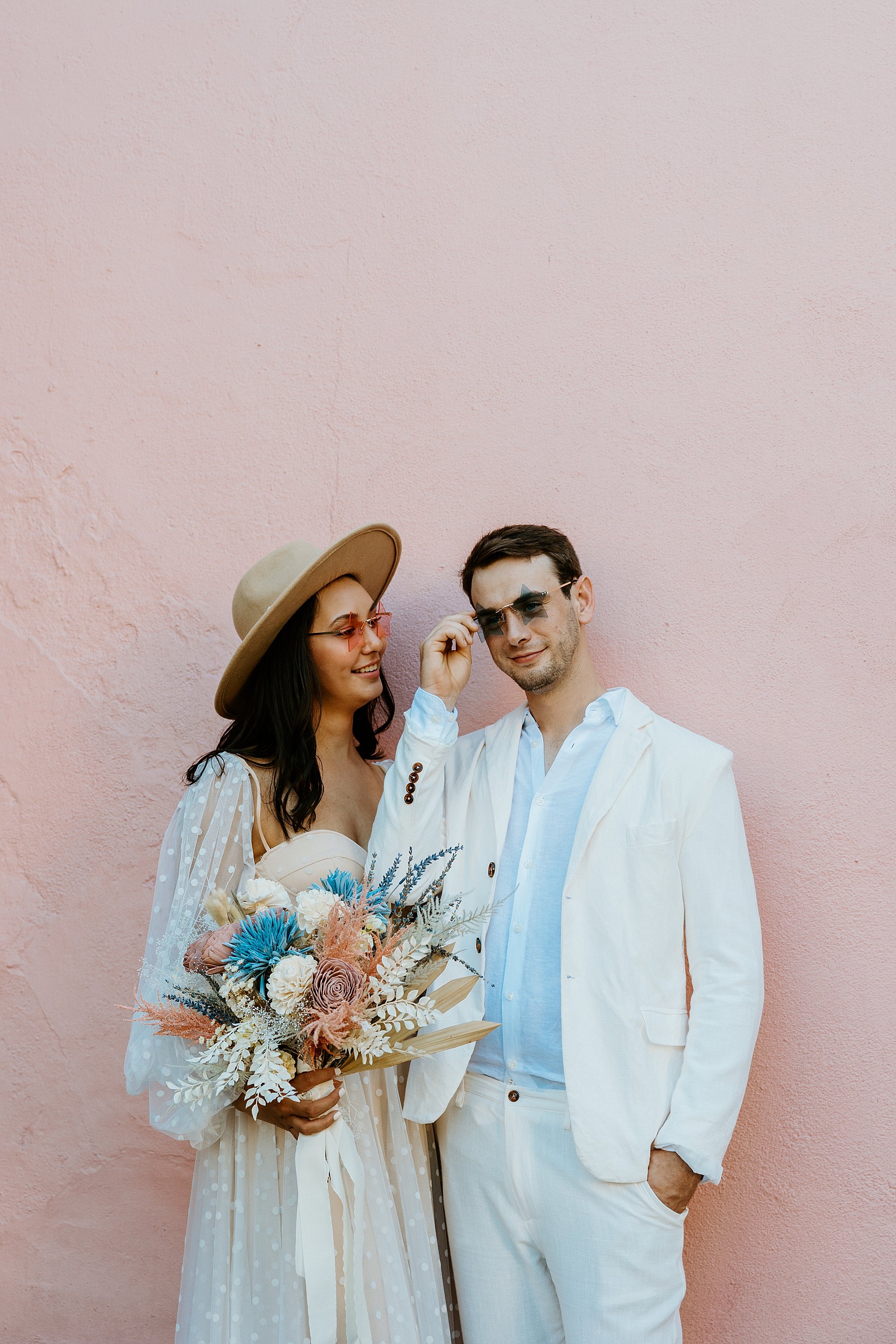 Couple stands together with cool star sunglasses that match the pink and blue houses on Rainbow Row