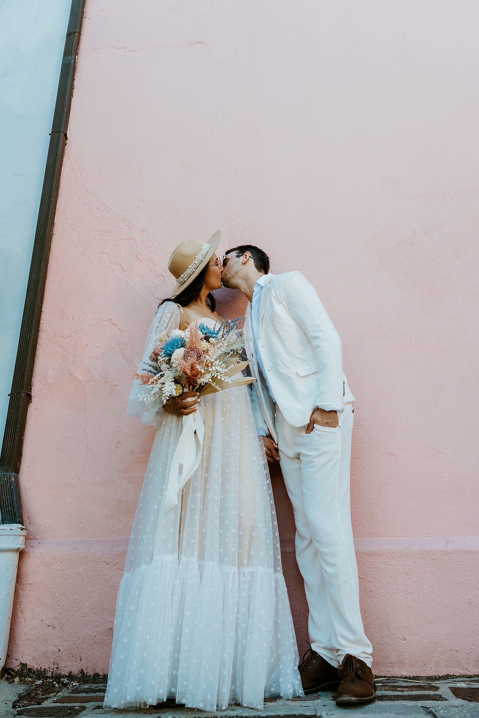 Couple kisses in front of a pink house on Rainbow Row in Charleston SC before they elope