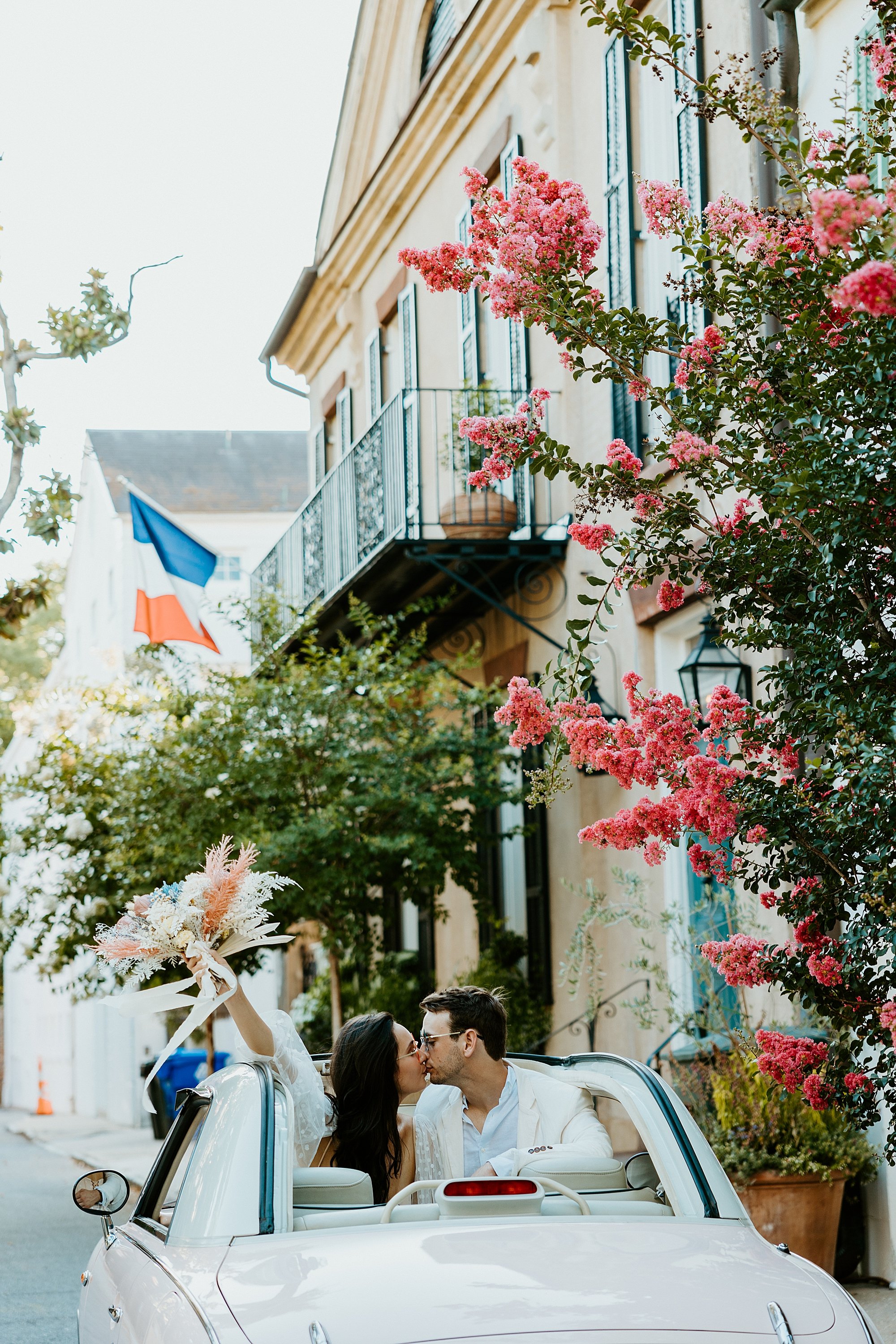 Couple kiss while in The Pink Figgy car among historic Charleston SC homes.