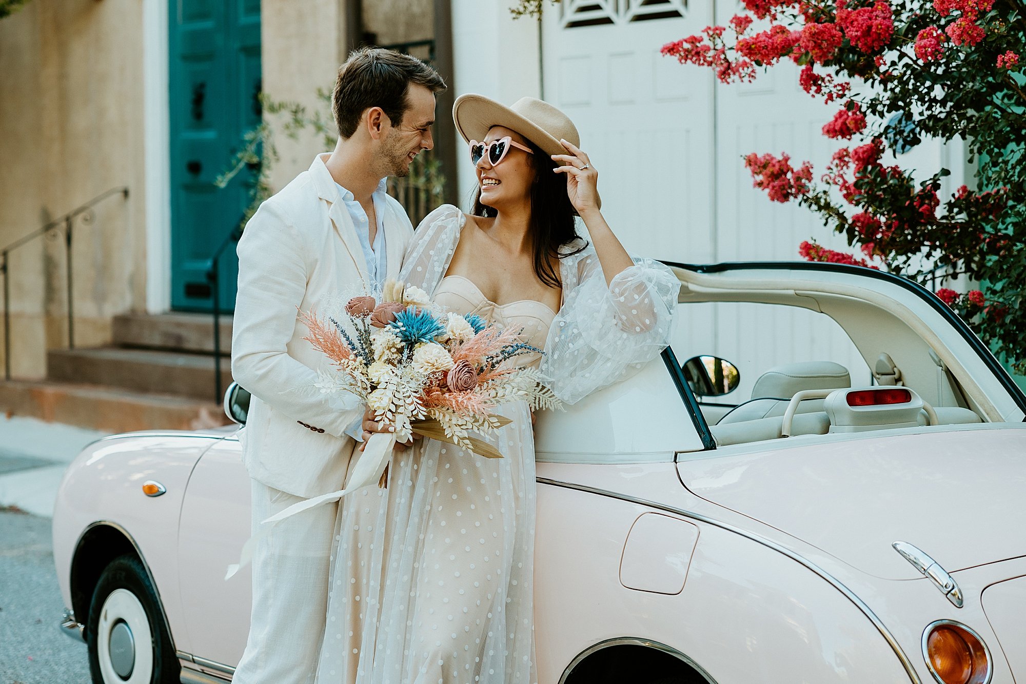 Couple stands together and leans agains The Pink Figgy car as they look at each other fondly.