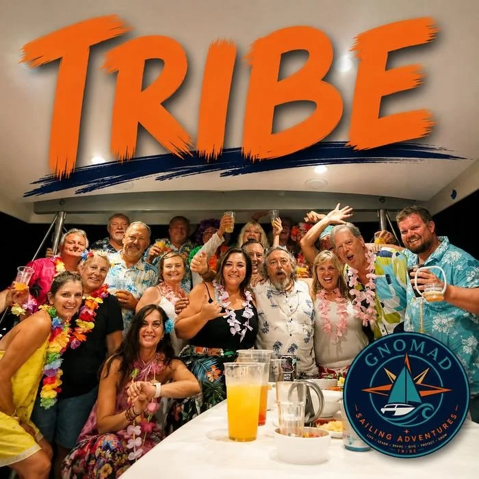 Group of people enjoying a party on a boat, many wearing leis, with a large sign reading 'TRIBE' above them and a logo for Gnomad Sailing Adventures at the bottom right.