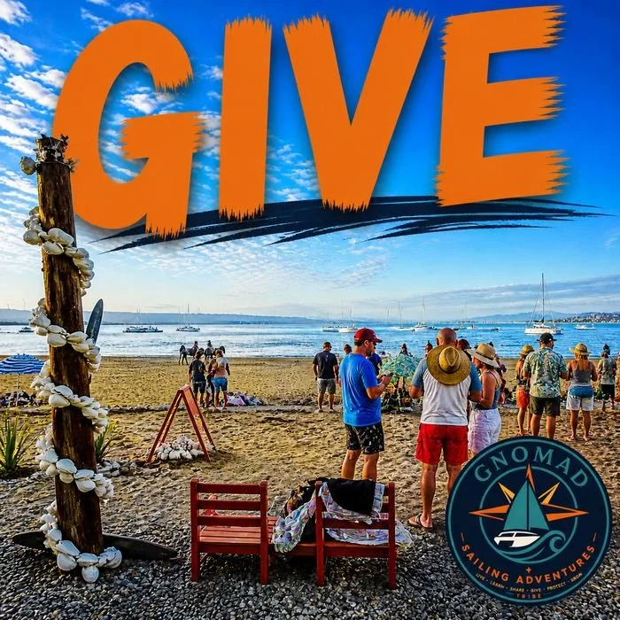 Beach scene with people gathering, boats in the water, and an overlaid large orange text that reads 'GIVE'. There is a decorated wooden post on the left with shells, and a logo at the bottom right for GNOMAD Sailing Adventures.