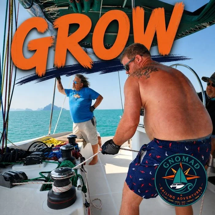 Two men on a boat, one shirtless wearing sunglasses and patterned shorts, the other in a blue T-shirt and khaki shorts, adjusting sails or ropes. Large orange and black sign reading 'GROW' is overhead, with a logo for GnOMAD sailing adventures.