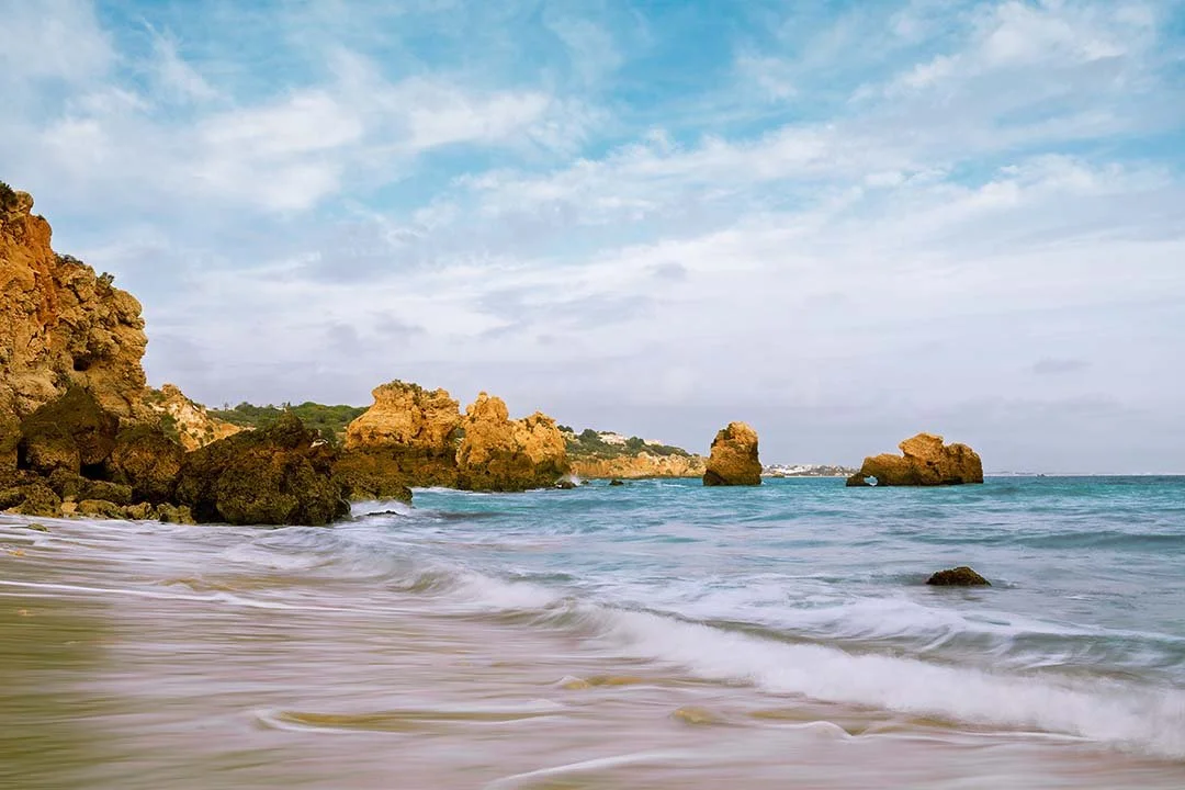 Waves moving around golden rock formations on a central Algarve beach