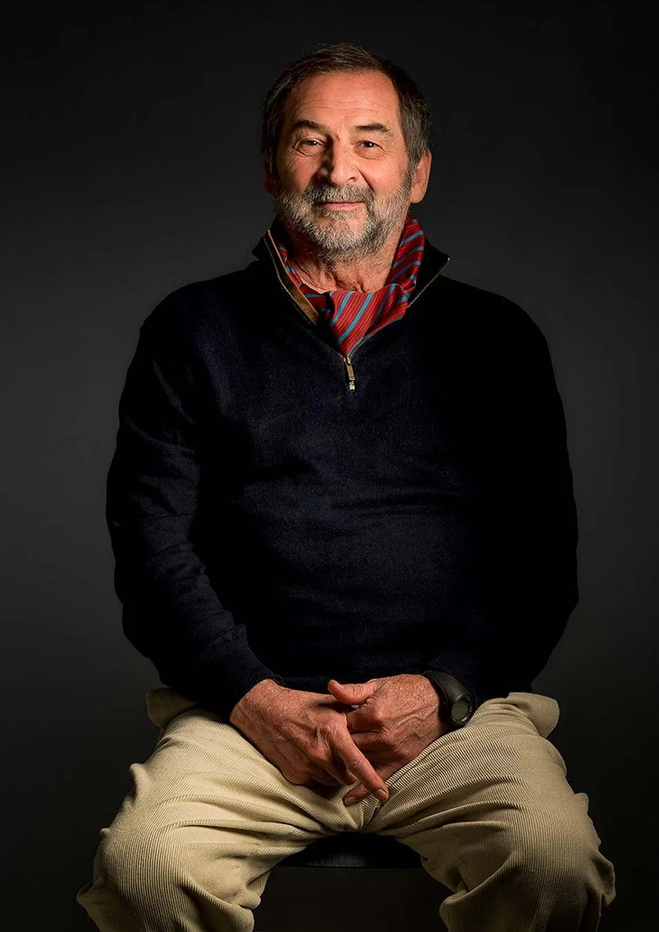 Contemporary studio portrait of an older man wearing a red scarf against a dark background