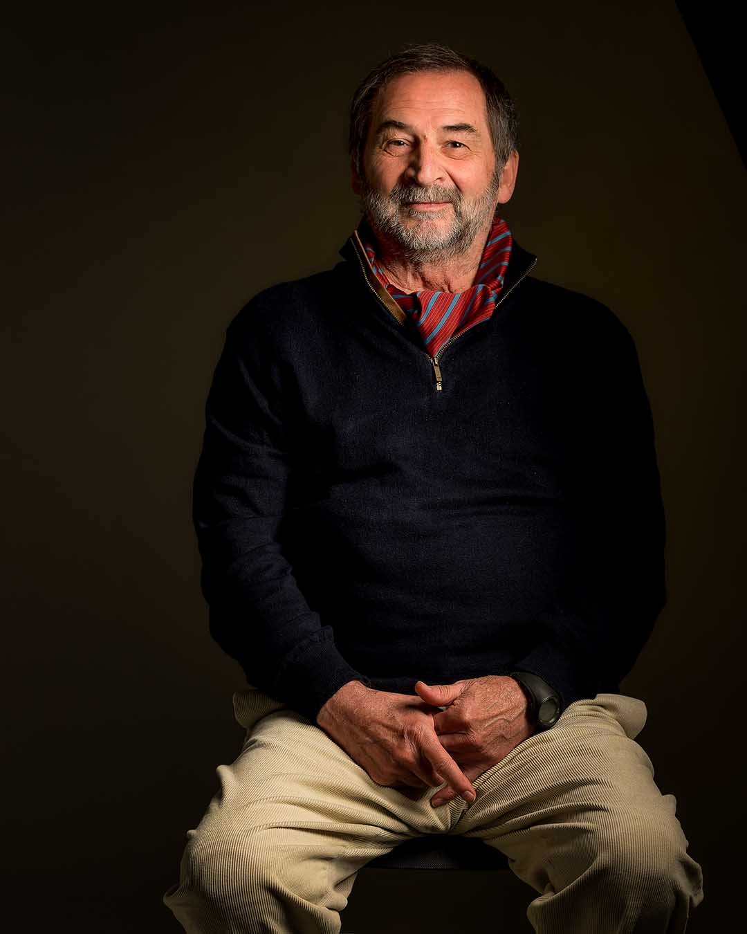 Studio portrait of an older man seated against a dark background