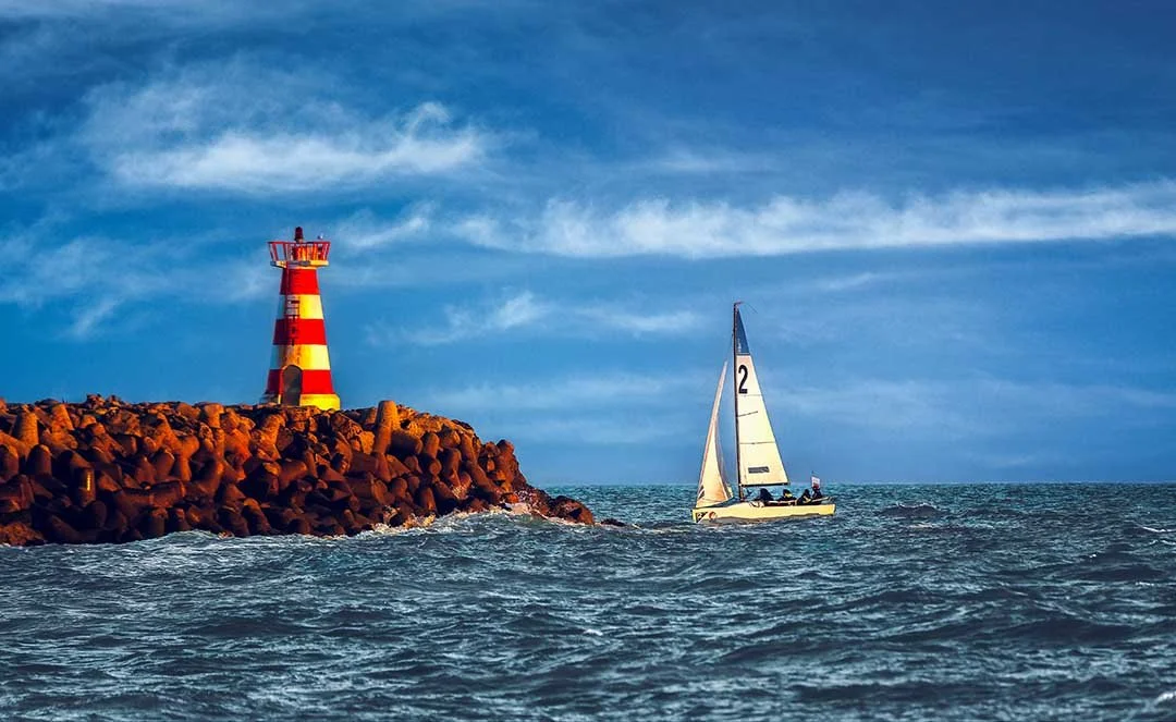 
Sailing boat passing the red and white lighthouse at Vilamoura Marina