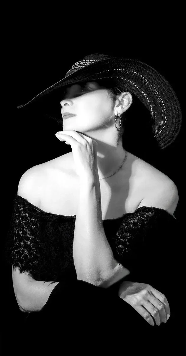 Lady seated in a Black & White image wearing an off shoulder free and a wide brimmed hat