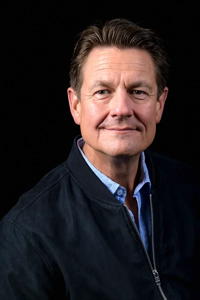 Professional studio headshot of a man against a black background