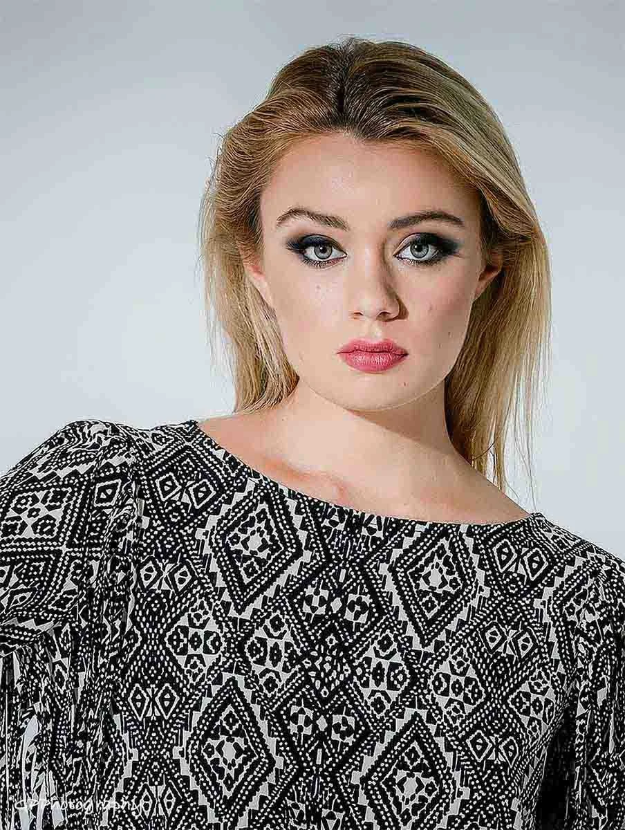 A young woman with blonde hair and blue eyes wearing a black and white patterned top.