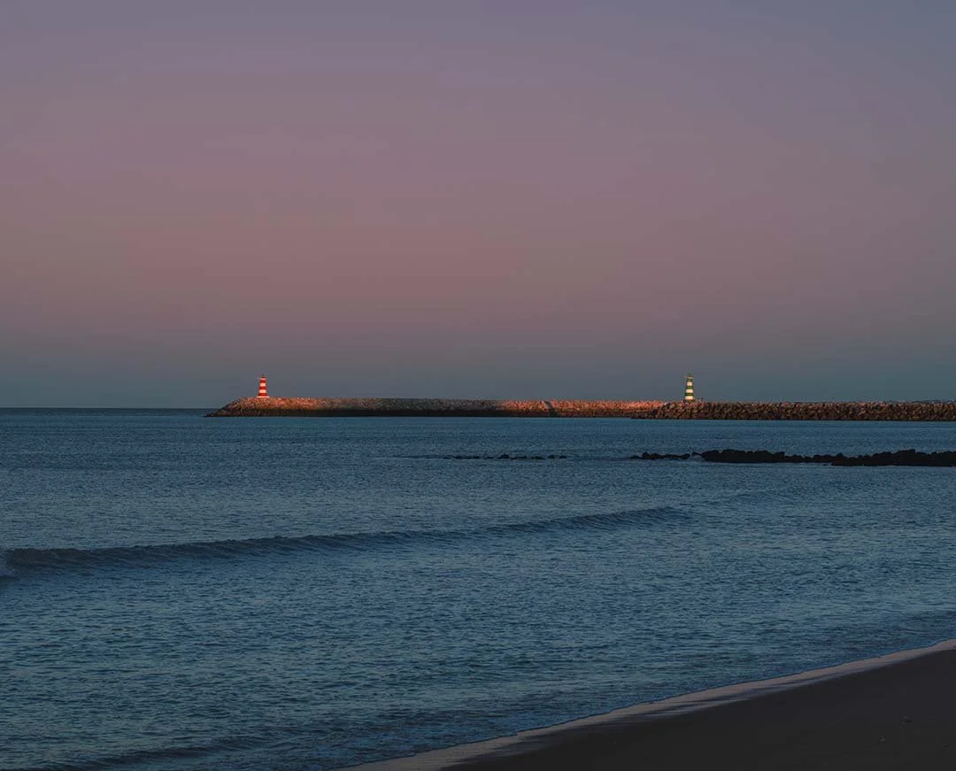 Red and green Vilamoura harbour lighthouses photographed across the sea before sunrise