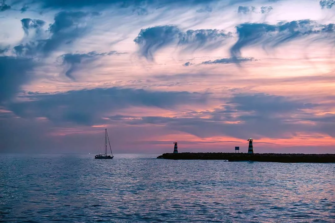 Sailing boat approaching Vilamoura harbour at sunset beneath dramatic cloud formations