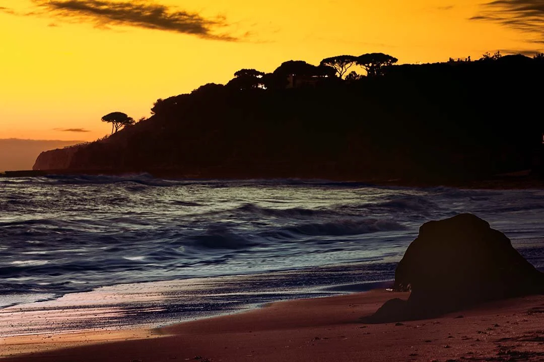 Waves and silhouetted cliffs at Olhos de Água during sunset