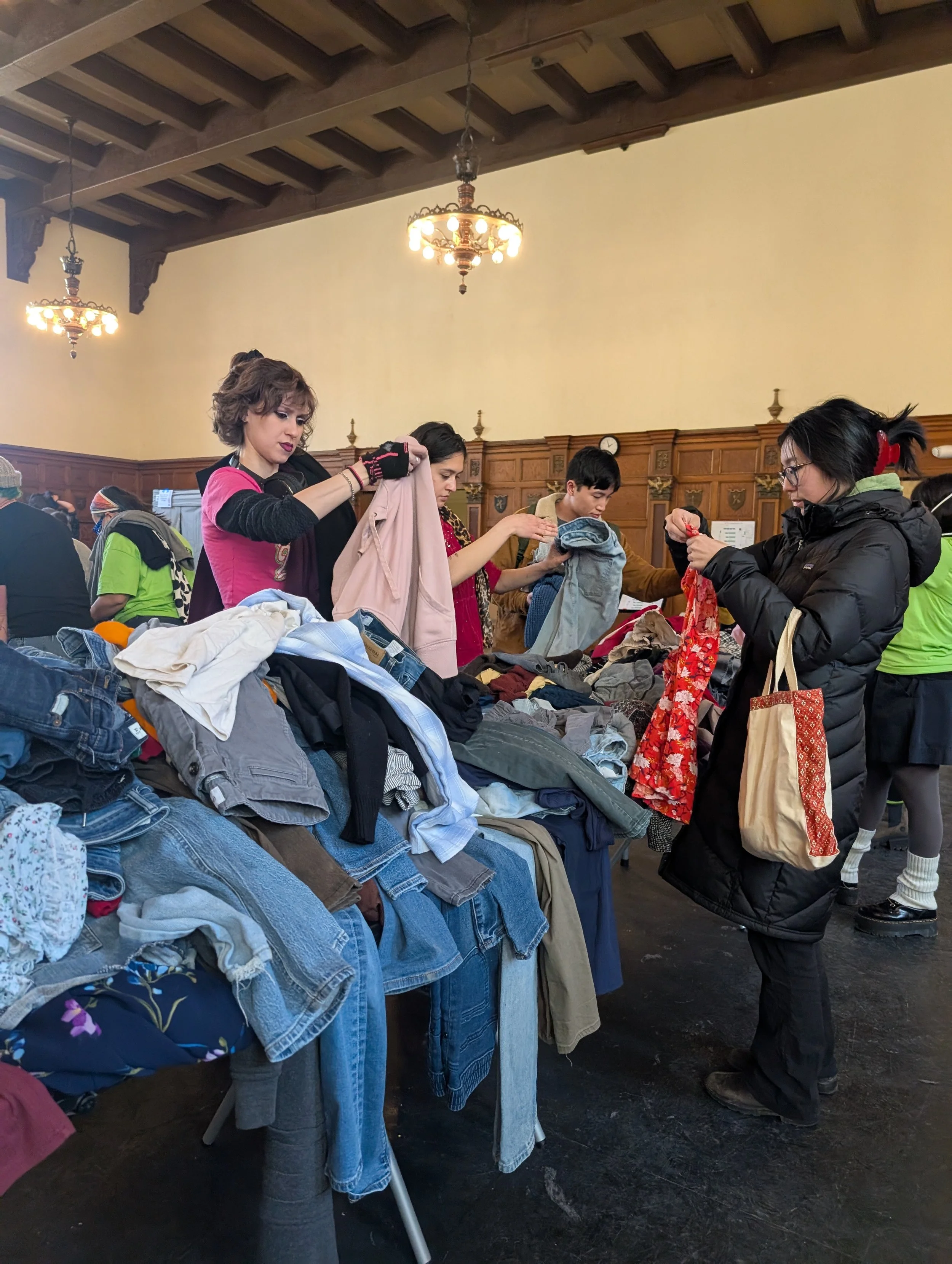 Several people sort through large piles of donated clothing at a swap