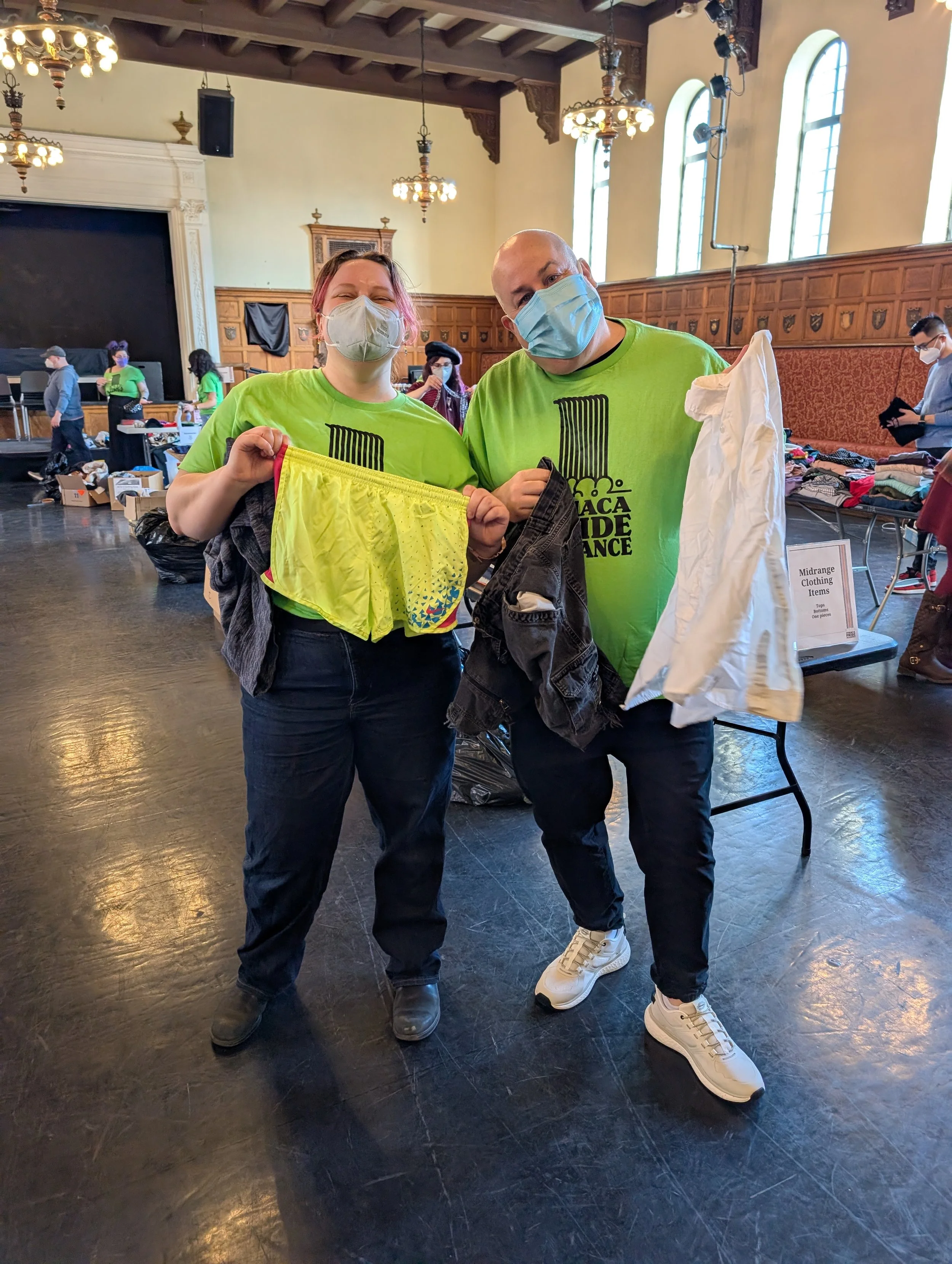 Two volunteers wearing N95 masks hold up clothing at a clothing swap