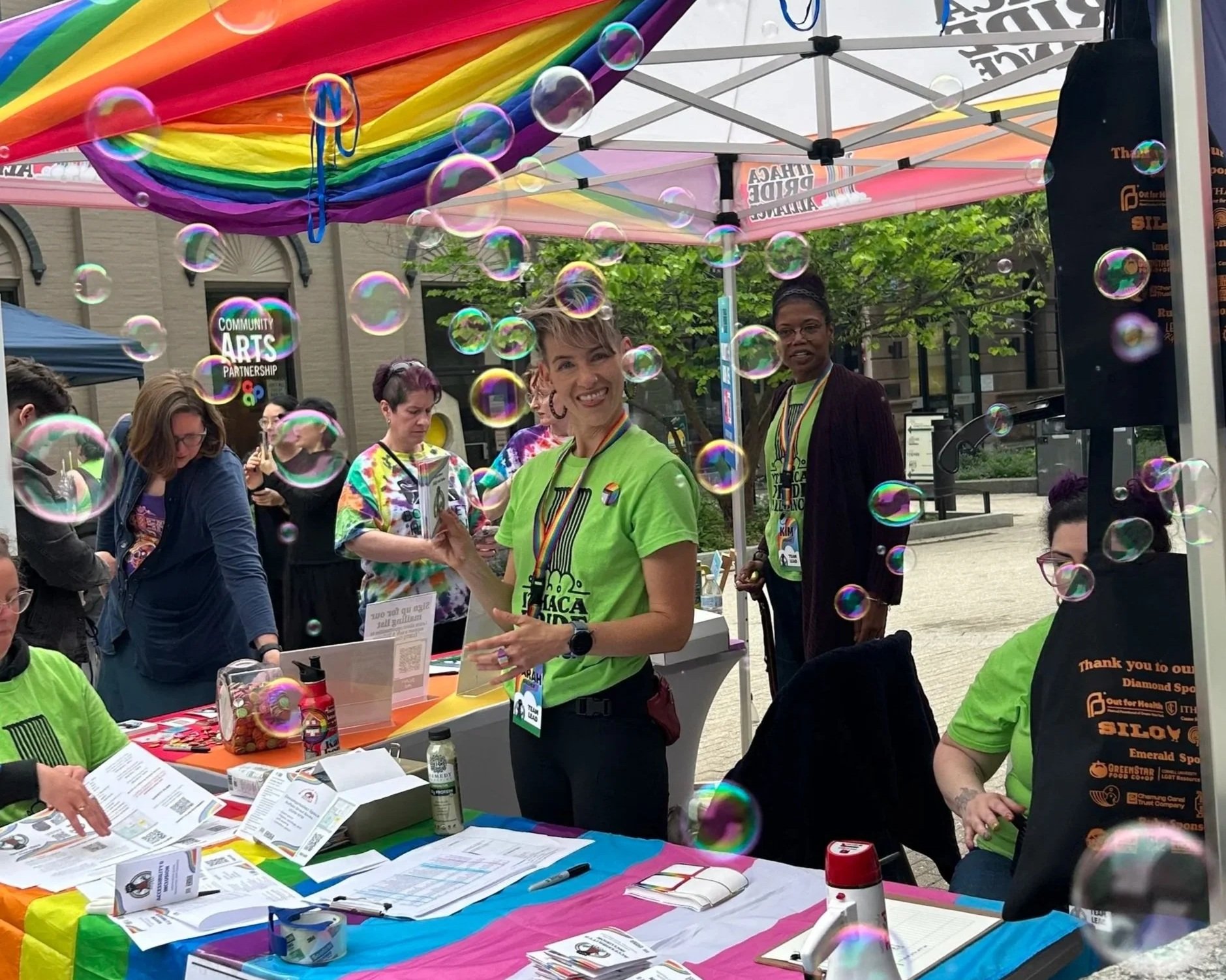 Volunteers wearing ithaca pride alliance t-shirts smile at the camera with bubbles in the foreground