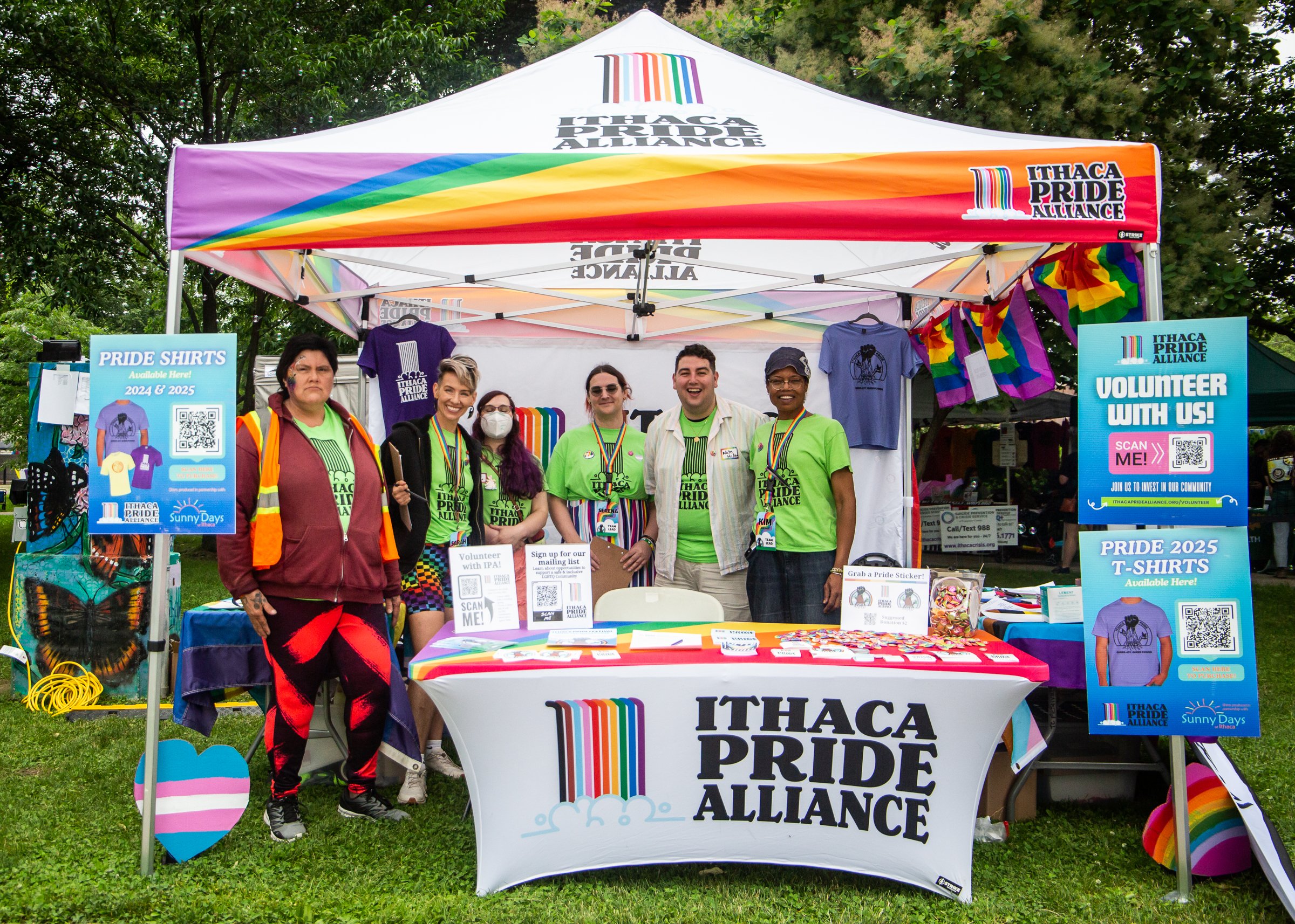 A group of volunteers some wearing masks pose in a main pride check-in tent with rainbow attire and decor