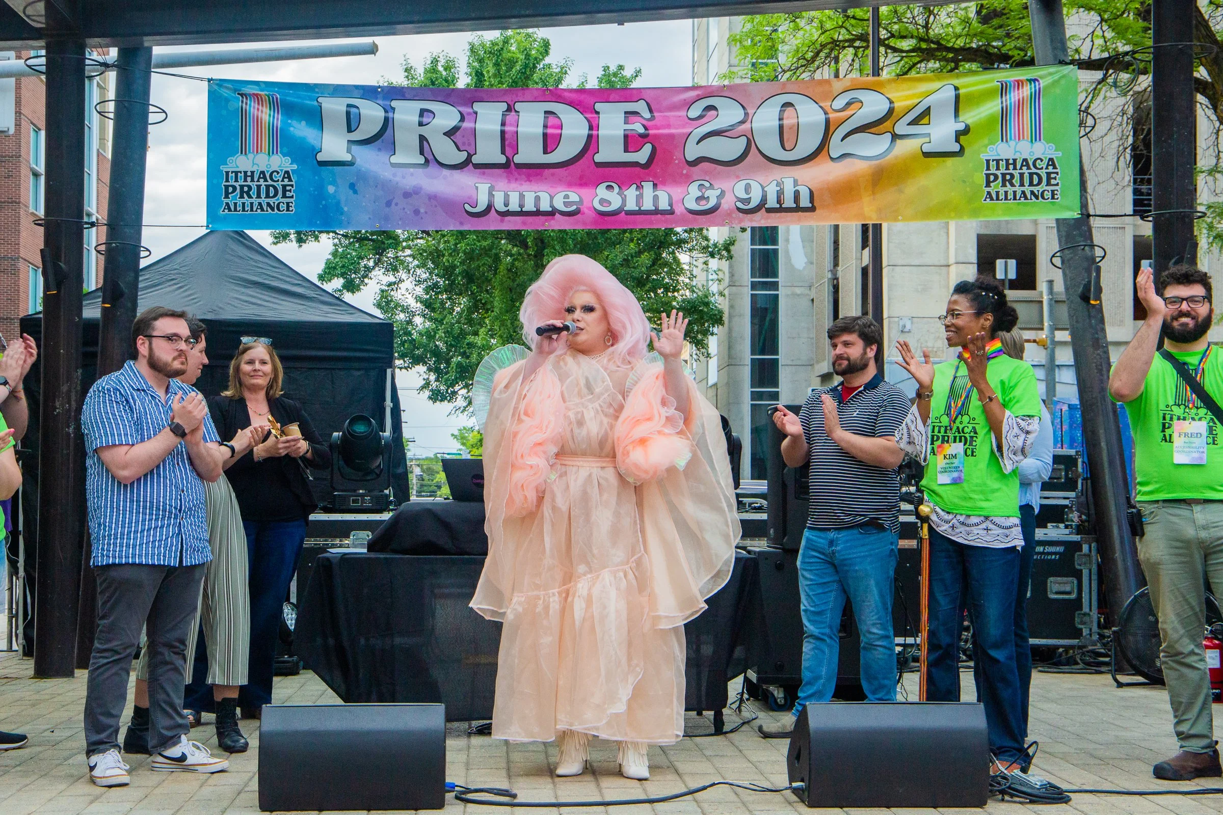 A drag queen and and clapping volunteers on a stage
