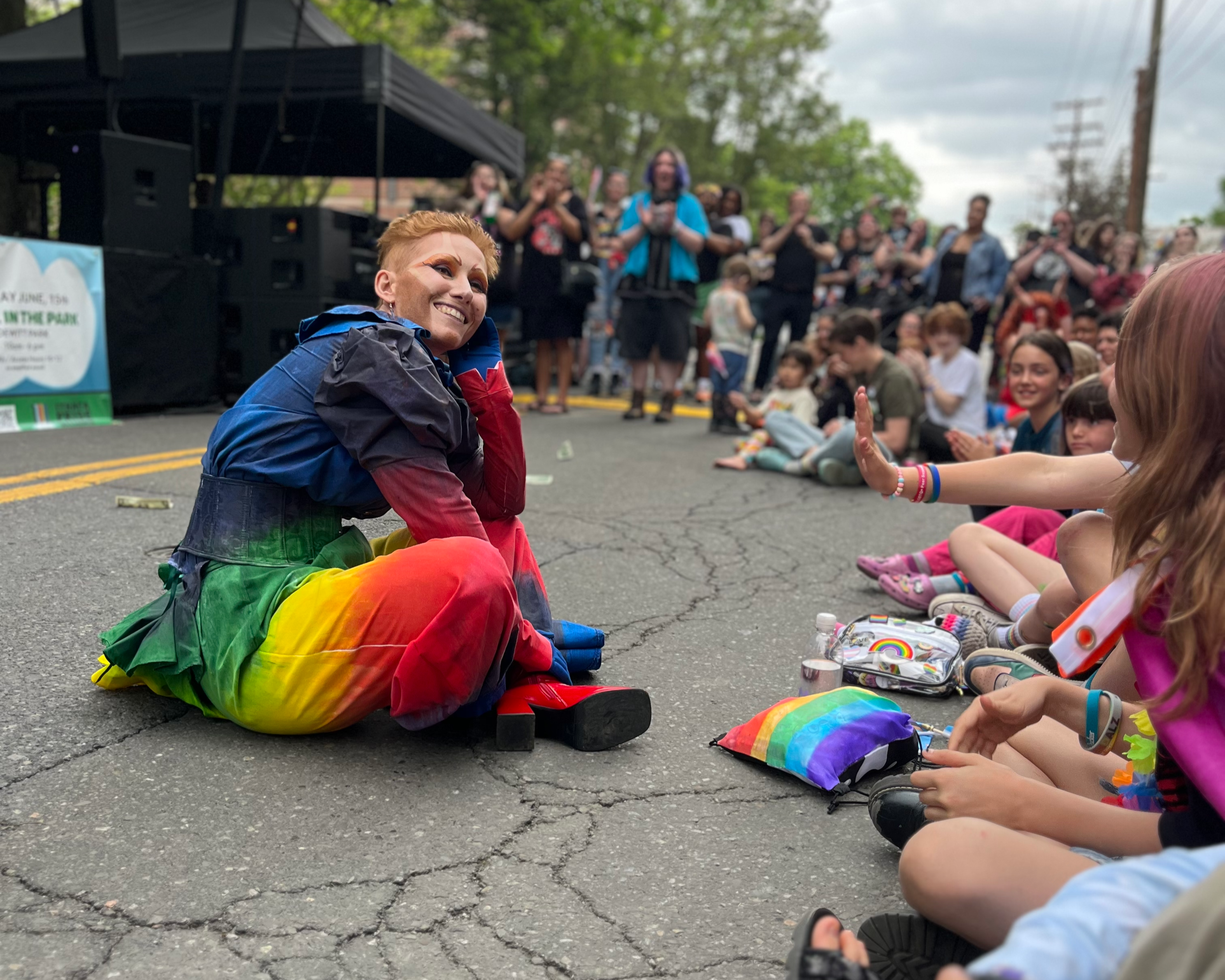 A person in drag smiles at a group of children watching