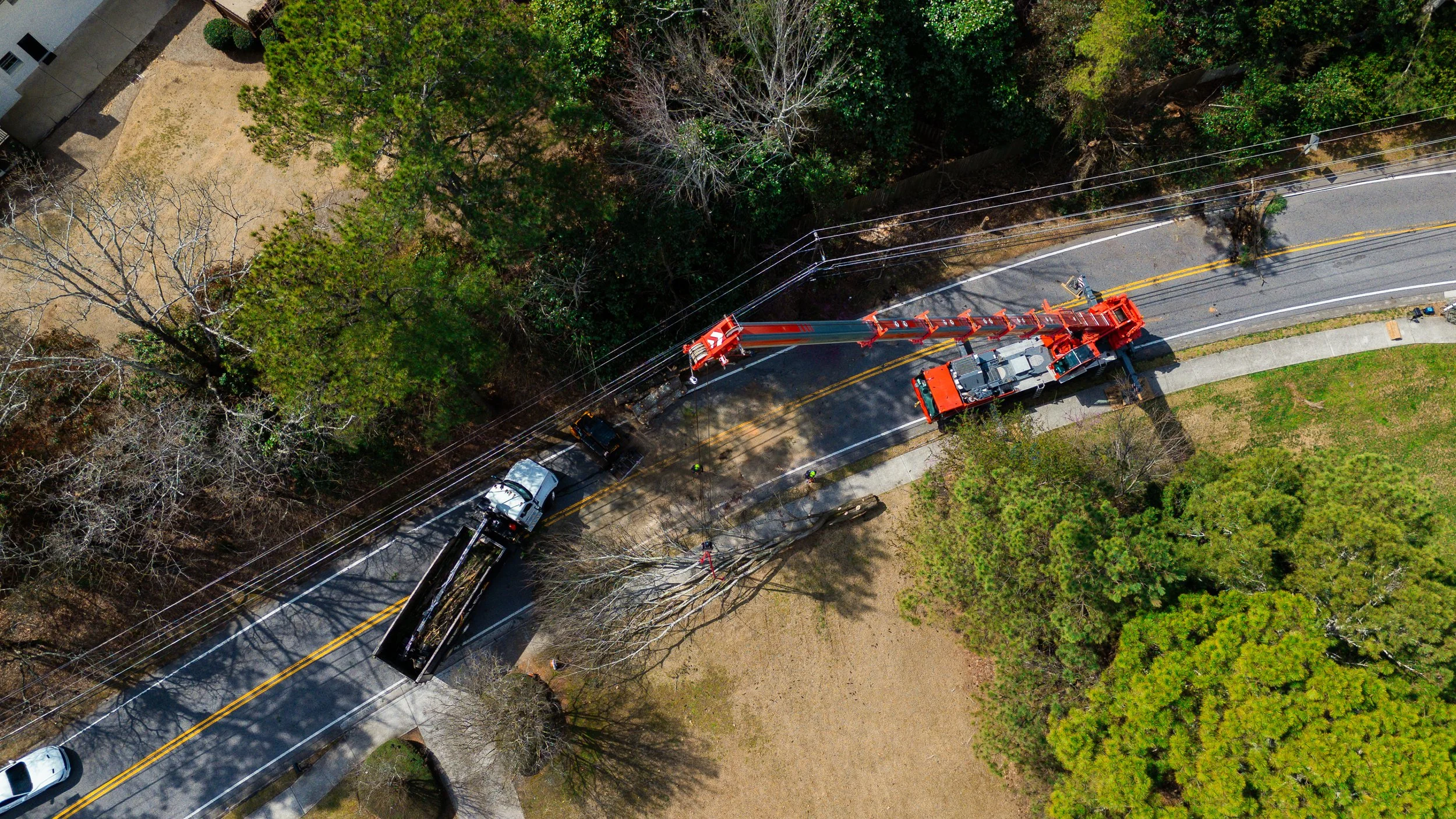 An aerial view shows a utility truck with a cherry picker working on power lines along a residential street bordered by trees, some leafless, on a sunny day. Beasley Tree Experts North Georgia, Metro Atlanta, Cherokee County