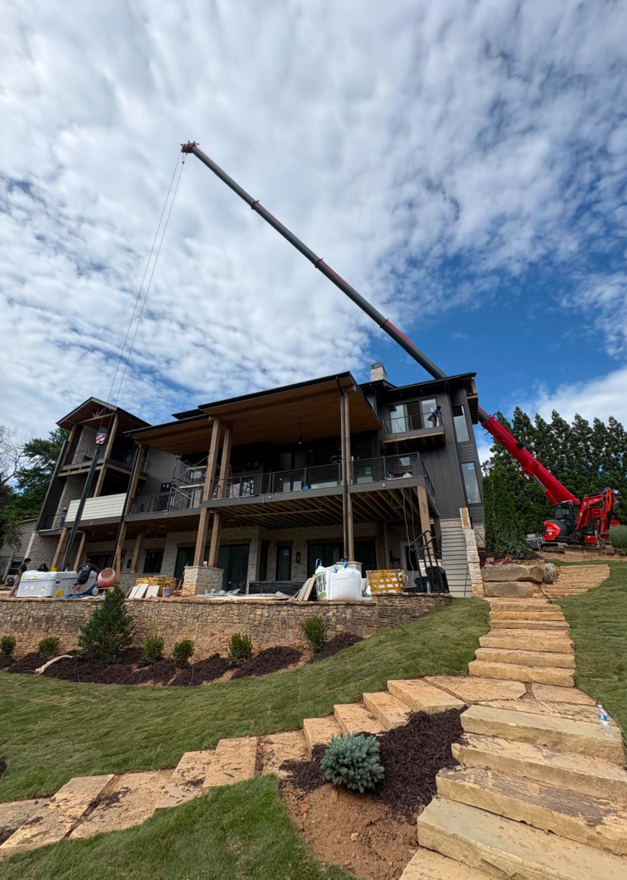 Crane extended near a home with stone patio for precision tree removal