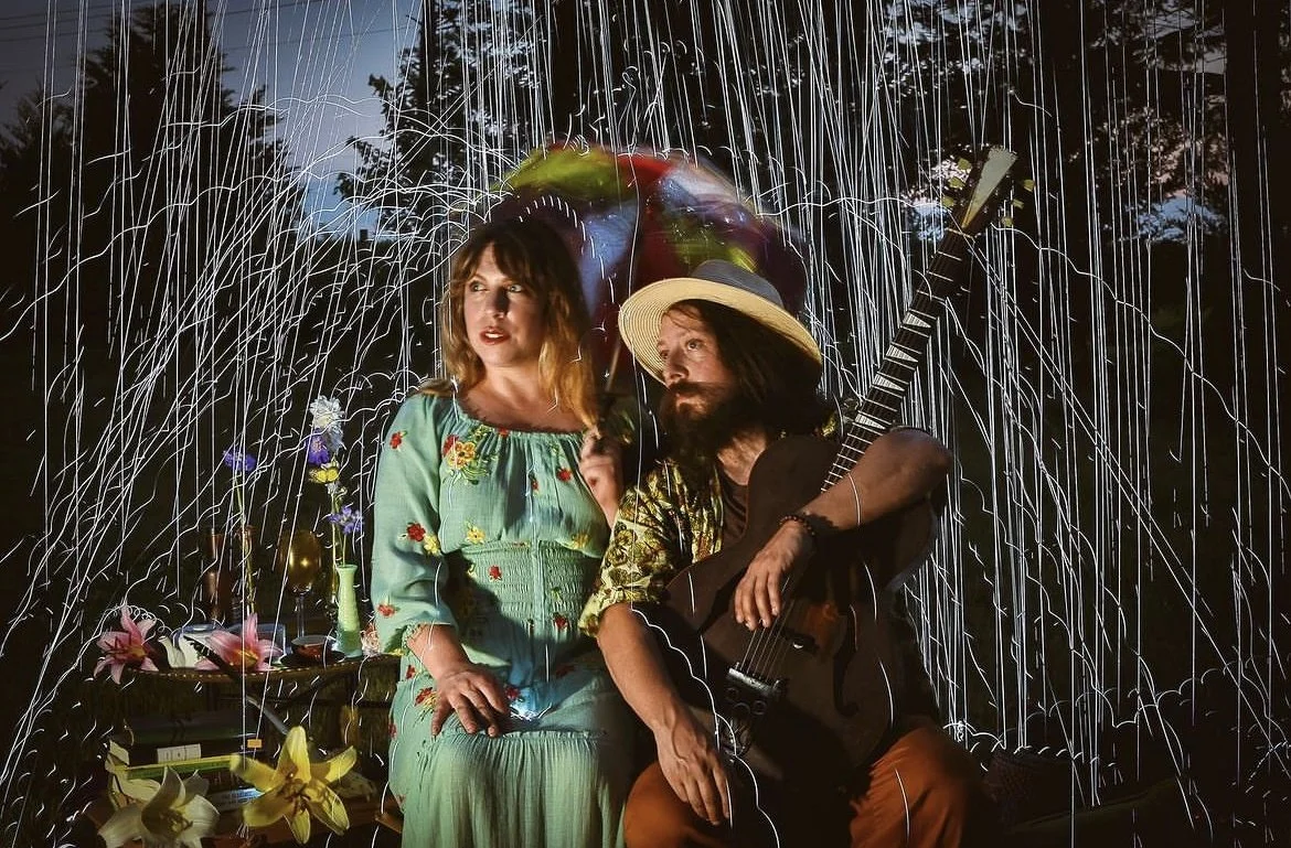 A musician duo: a woman in a blue dress with flowers and a man holding a guitar