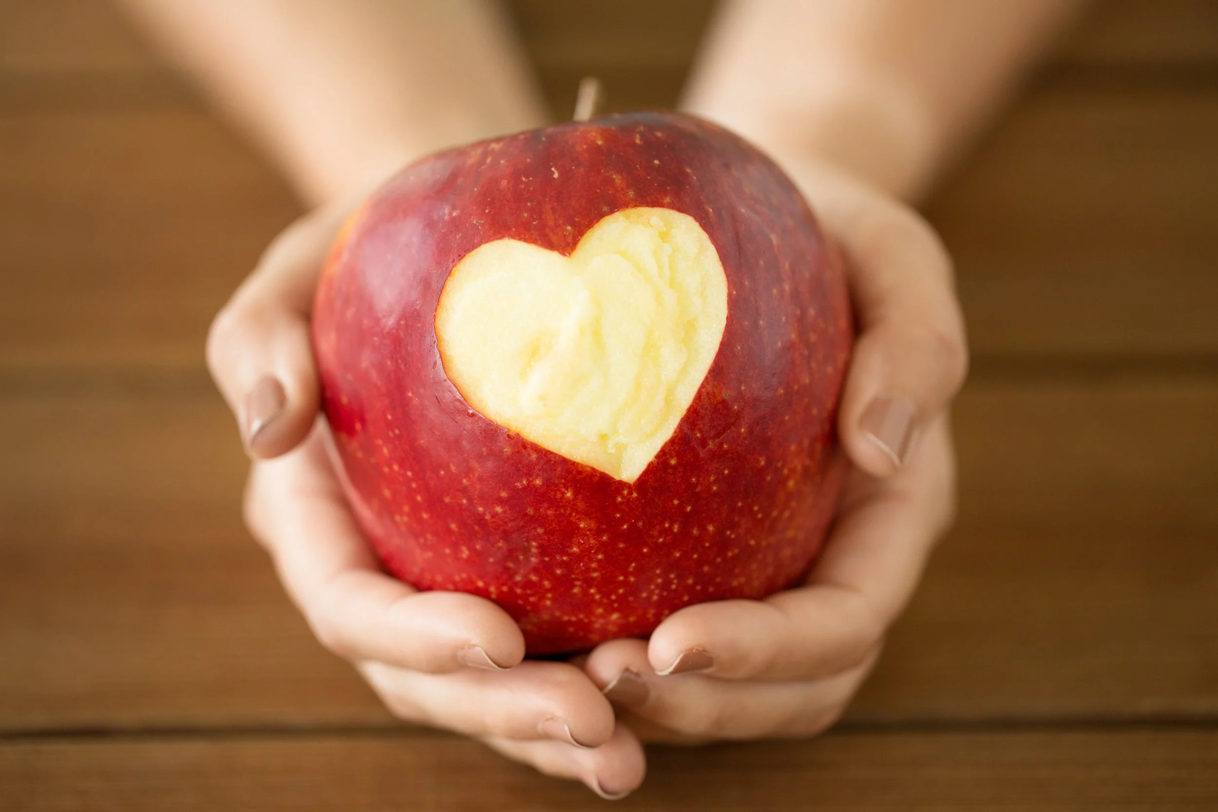 A person holding a red apple with a heart-shaped carve revealing the yellow flesh inside.