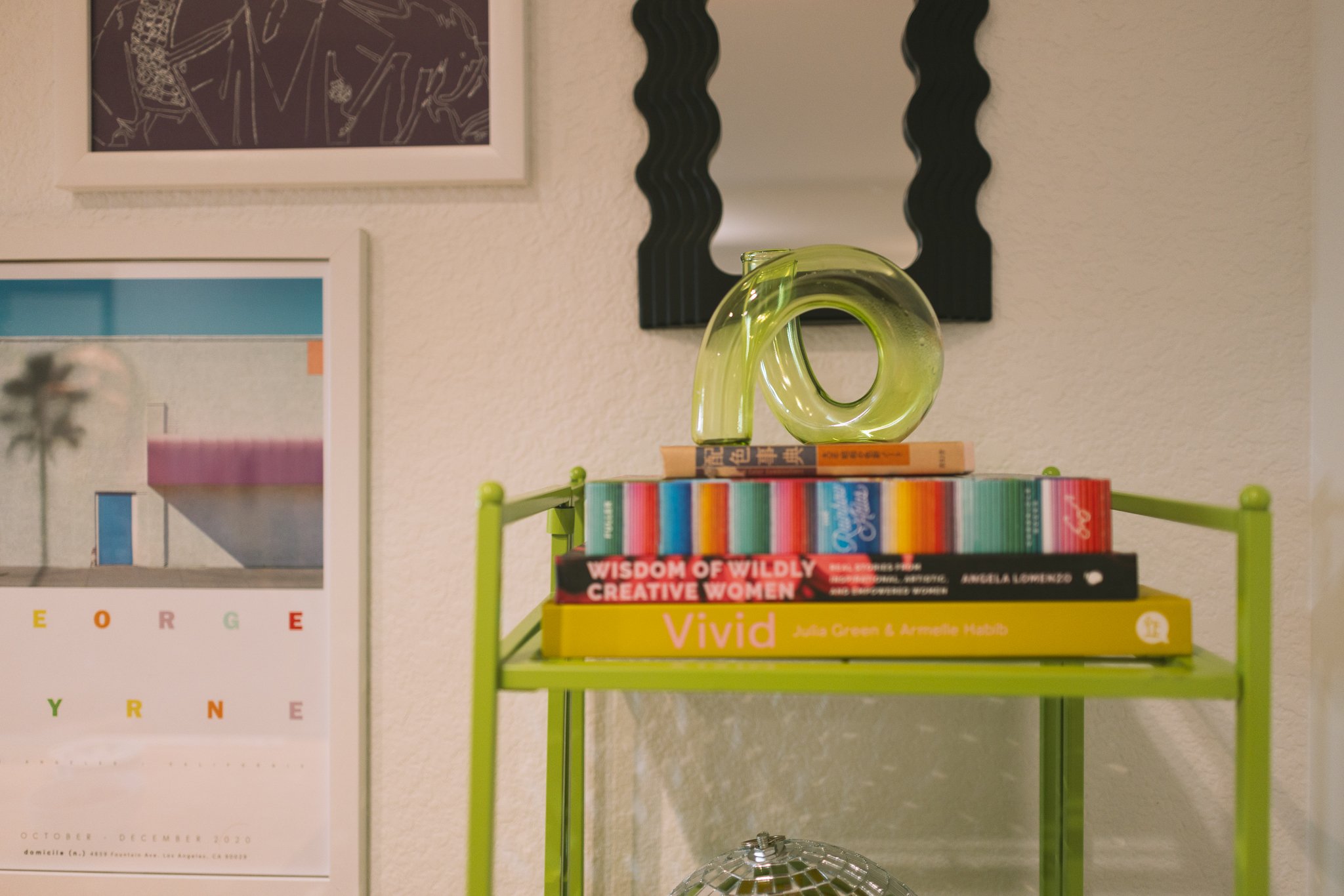 Colorful book and decor arrangement on a green shelf with modern artwork on the wall.