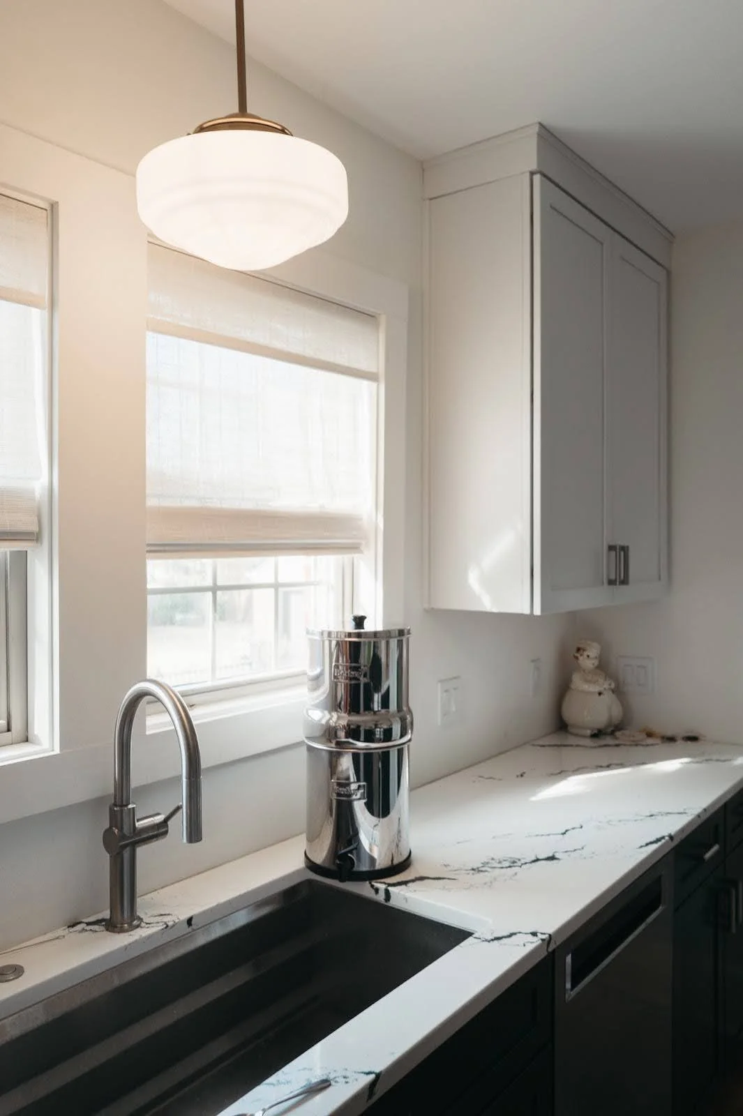 Modern kitchen with farmhouse sink, marble countertops and natural light from window, highlighting clean and functional design