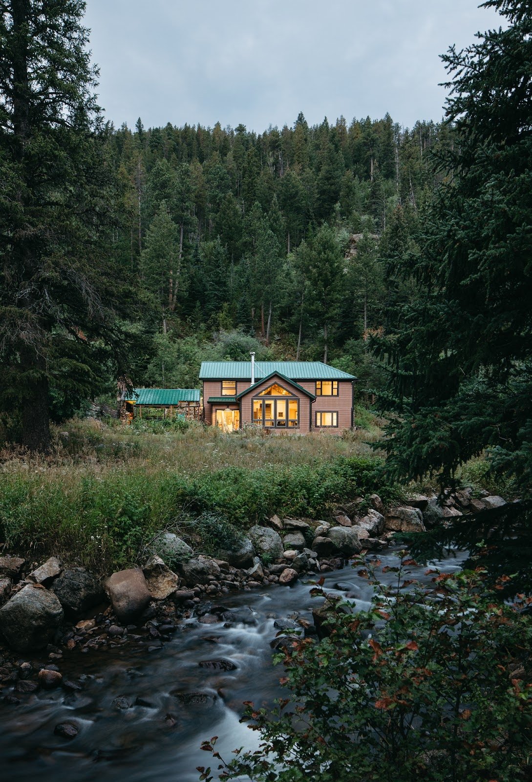Mountain home surrounded by forest with a creek in the foreground, highlighting a secluded residential setting in nature