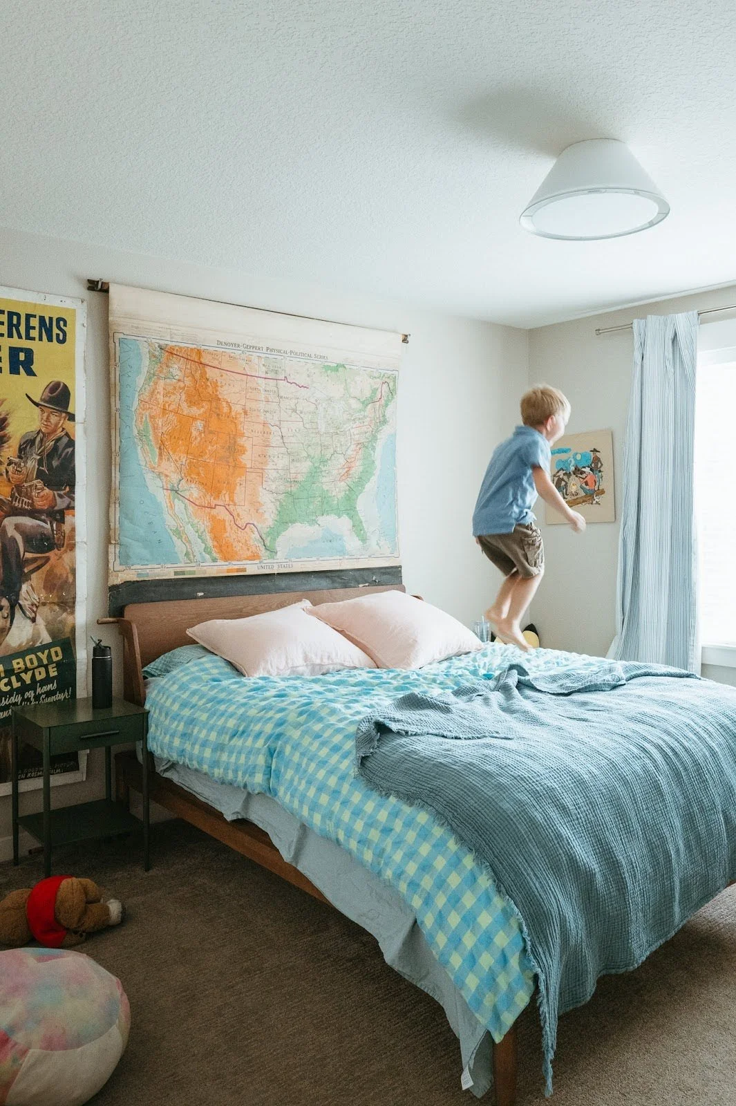 Child jumping on a bed in a bright bedroom with vintage map artwork, capturing a candid moment of everyday home life