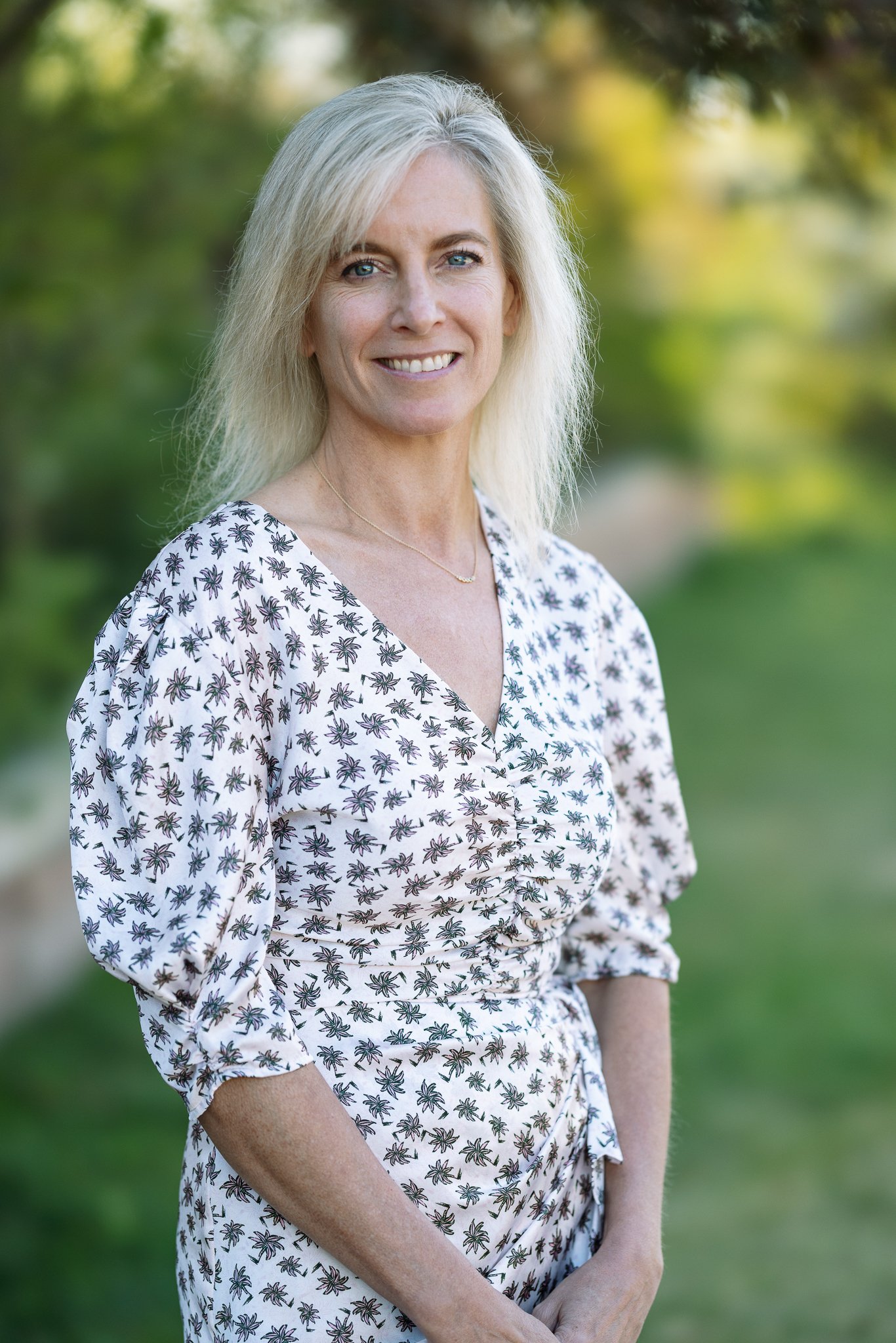 Smiling woman with blonde hair wearing a floral dress standing outdoors